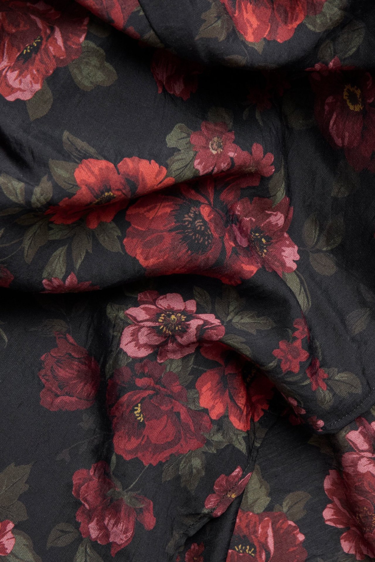 Zbliżenie czarnego materiału sukienki w kwiaty z dużymi czerwonymi i różowymi kwiatami oraz zielonymi liśćmi.