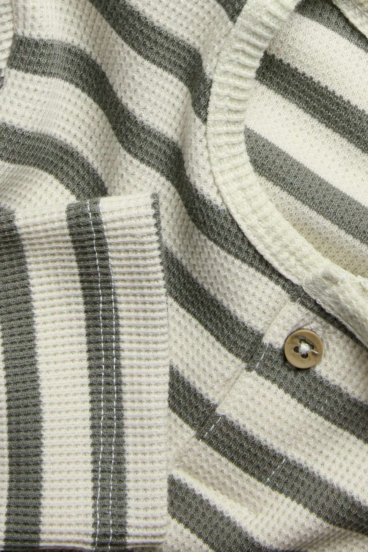 Zbliżenie: Pasiasta bluzka z dzianiny waflowej, kremowe, ciemnozielone paski, brązowy guzik.