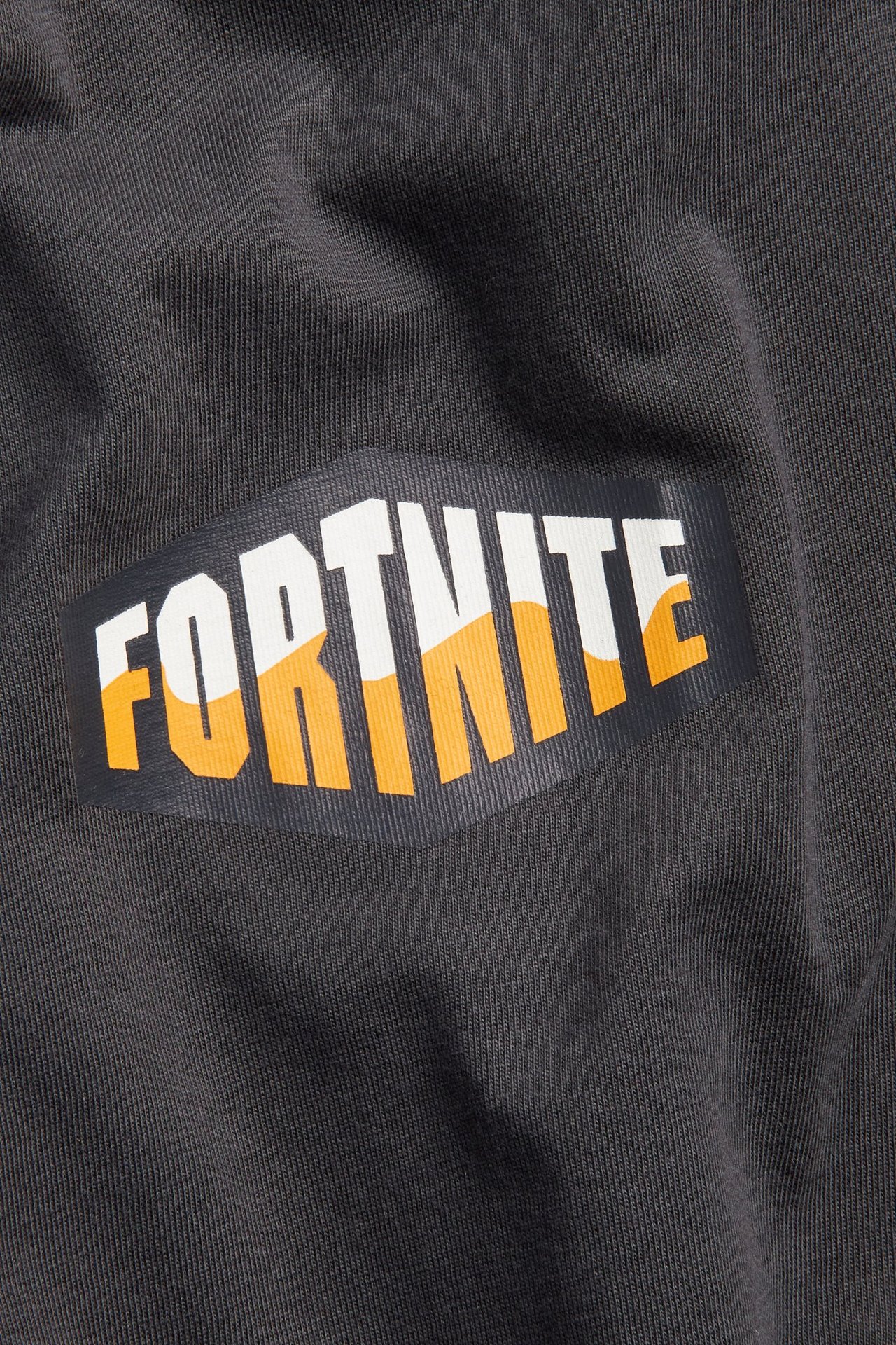 Zbliżenie na czarny bawełniany t-shirt z białym i pomarańczowym nadrukiem logo Fortnite z przodu.