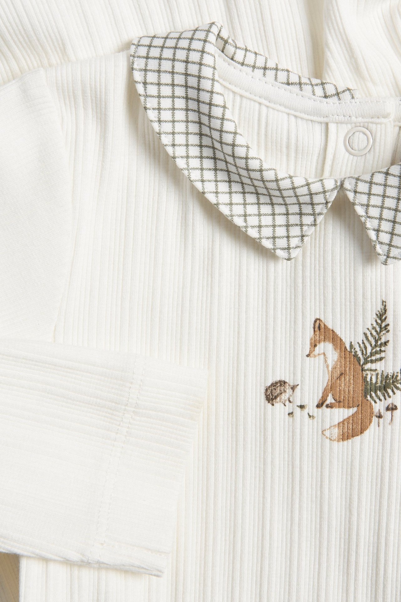 Lähikuva luonnonvalkoisesta ribbineuleisesta vauvan bodytista, jossa ruudullinen kaulus ja kettupainatus edessä.