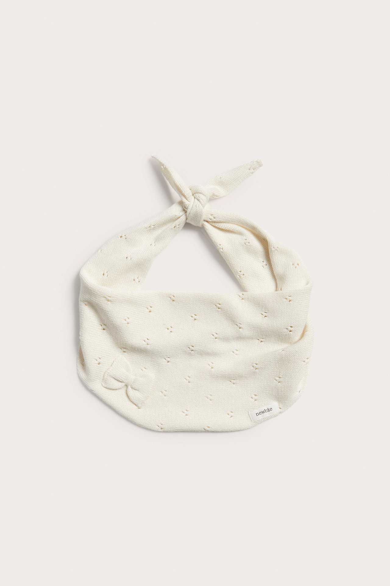 Widok z przodu: Ecru dziergany bawełniany szalik trójkątny z ażurowym wzorem i małą kokardką, zawiązany.