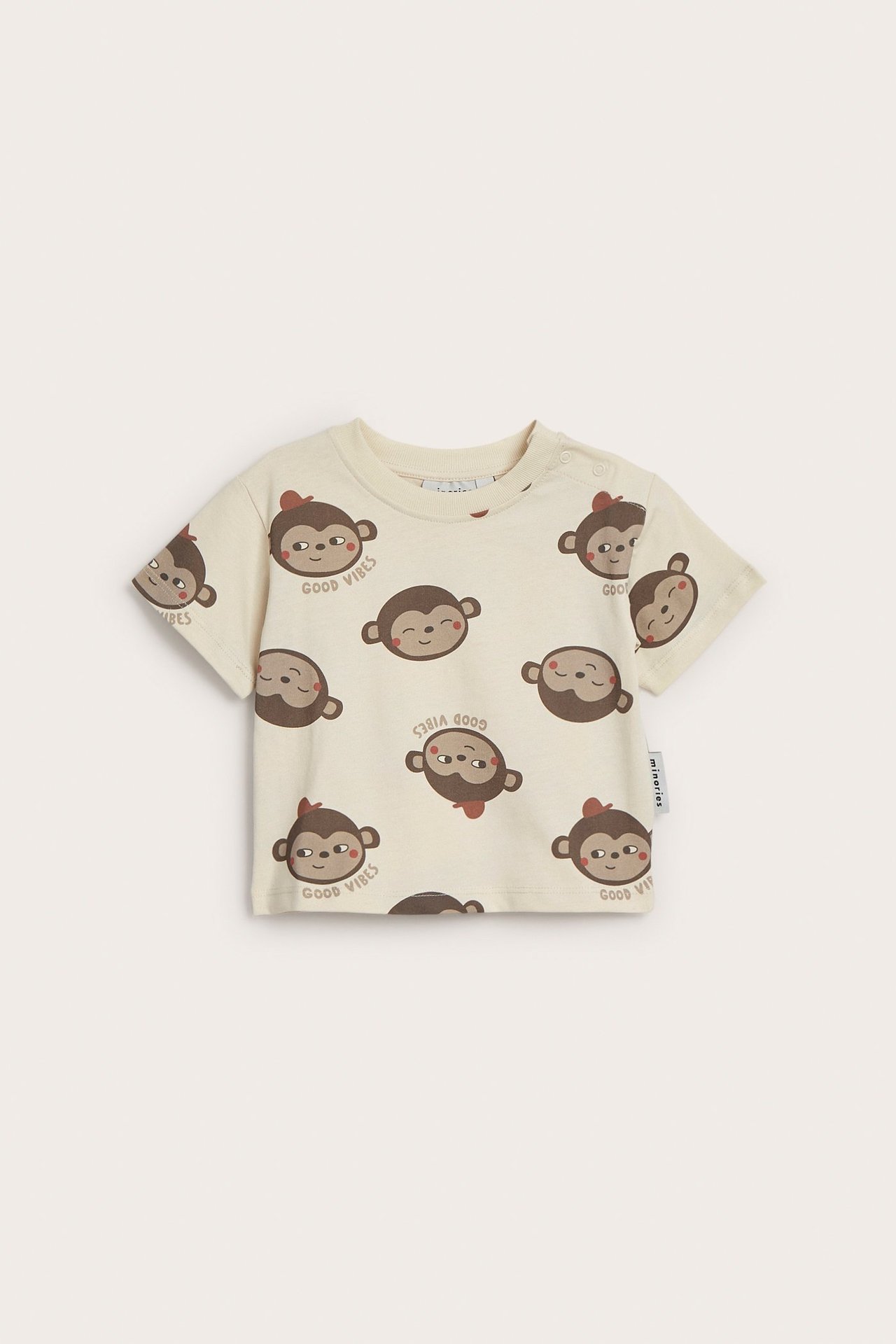 Edestä: vaaleanbeige puuvillainen vauvan t-paita, jossa apinakuvio ja olkapään nepparit.