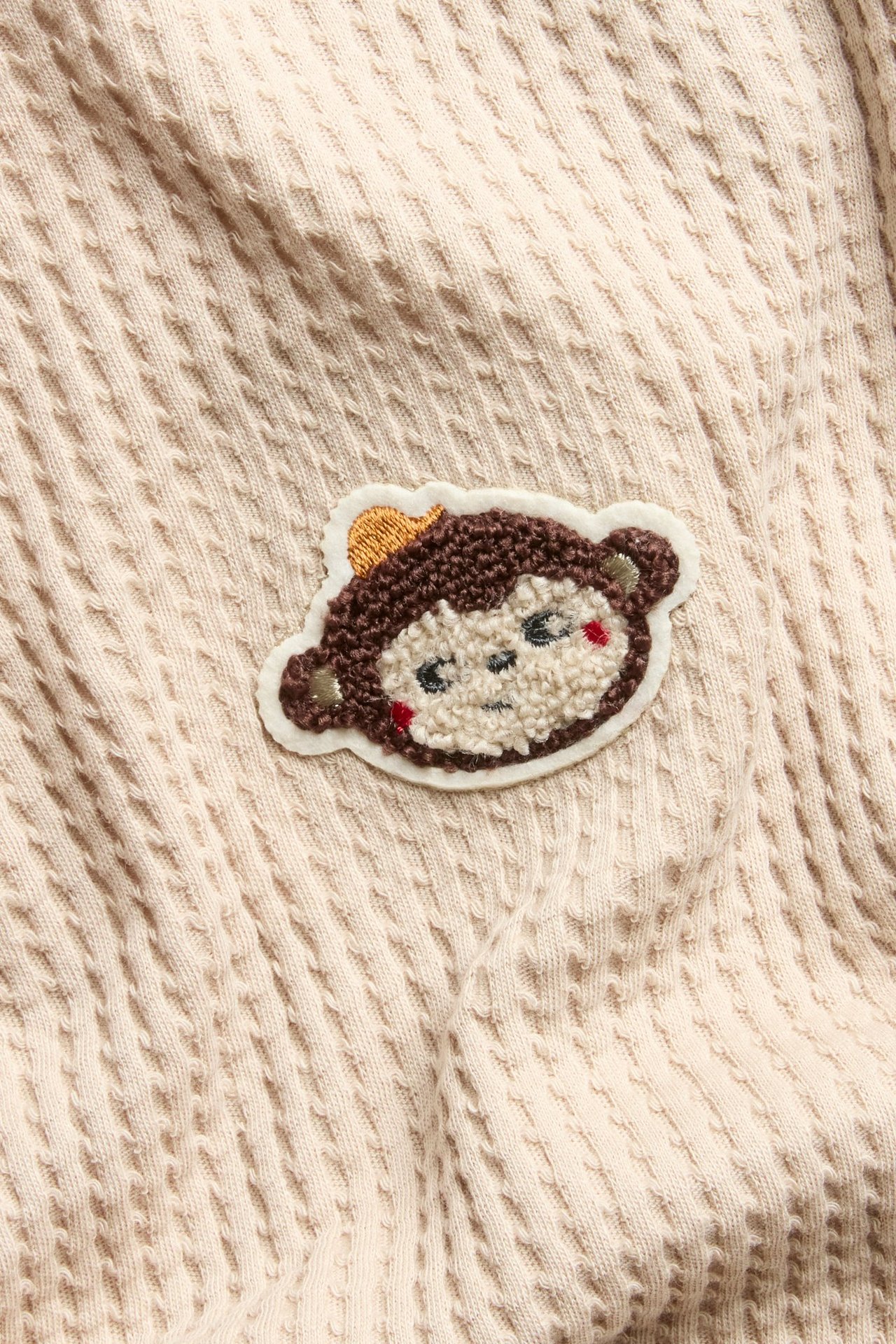 Zbliżenie beżowego bawełnianego T-shirtu z waflowej dzianiny z brązowym haftem małpy frotte.