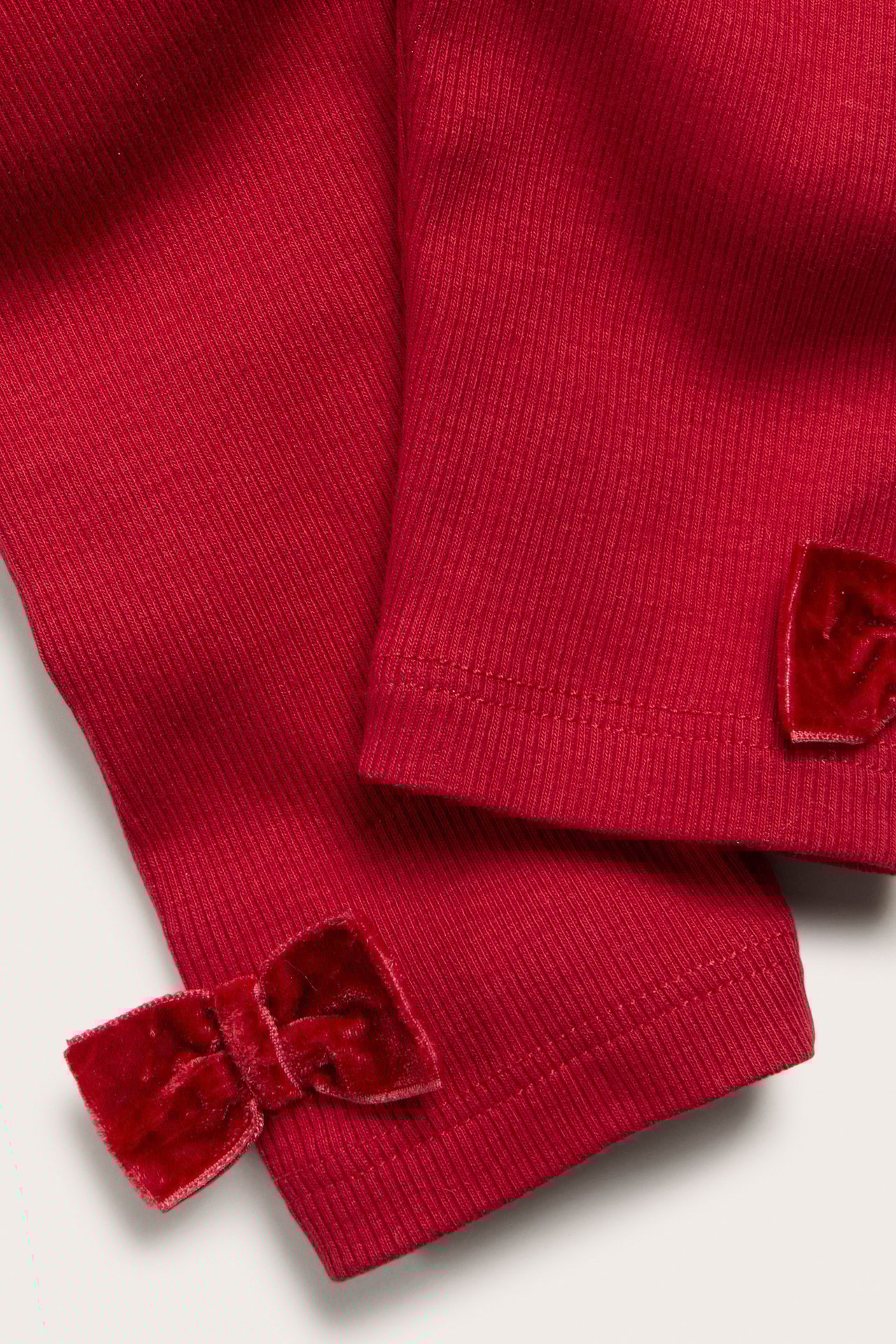 Zbliżenie na czerwone, prążkowane legginsy niemowlęce z aksamitnymi kokardkami przy kostkach.