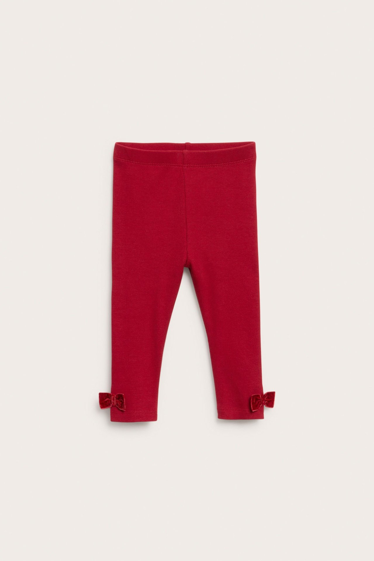 Frontbilde av røde ribbestrikkede baby-leggings med fløyelsløyfer ved anklene.