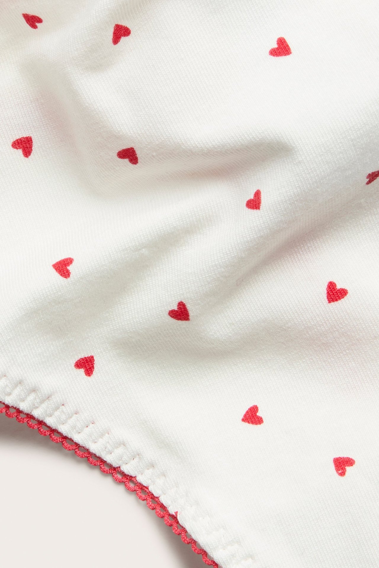 Nærbilde av offwhite bomullsstringtruse med små røde hjerter og rød picotkant.