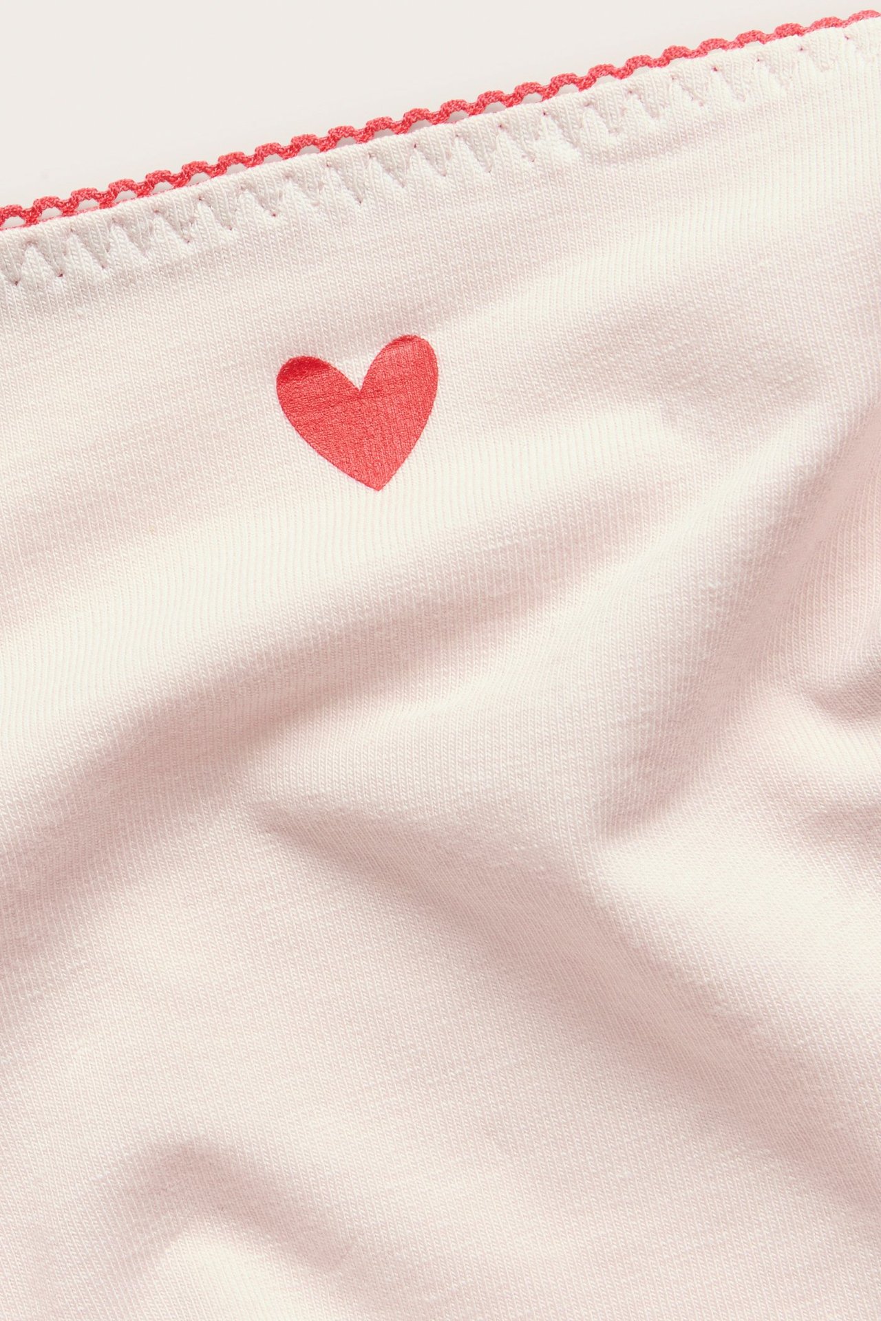 Nærbilde av en rosa bomullsstringtrusa med rødt hjerteprint og picot-strikkdetalj.