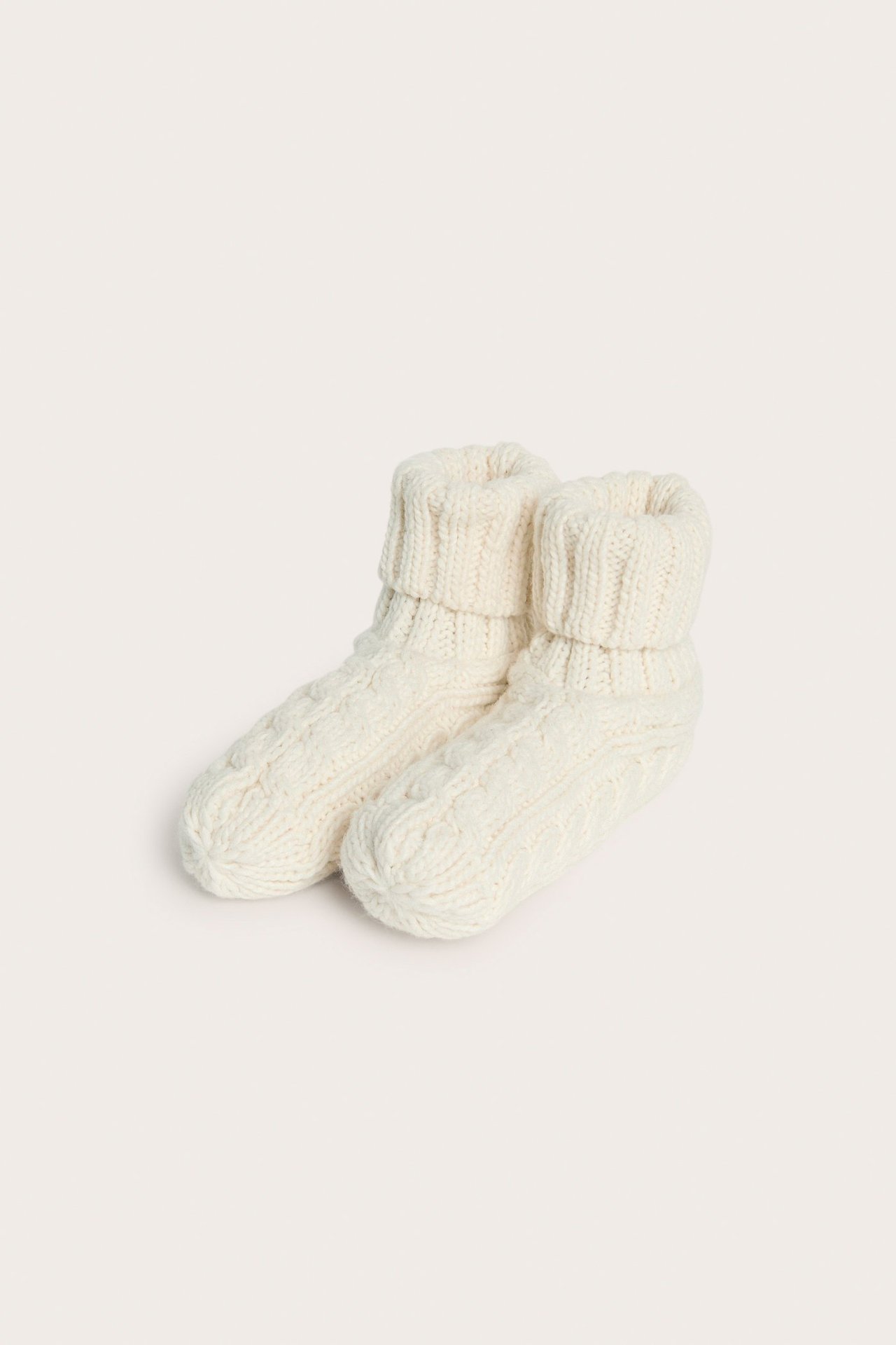 Widok z góry pary jasnobeżowych, warkoczowych kapci ze złożonymi mankietami.