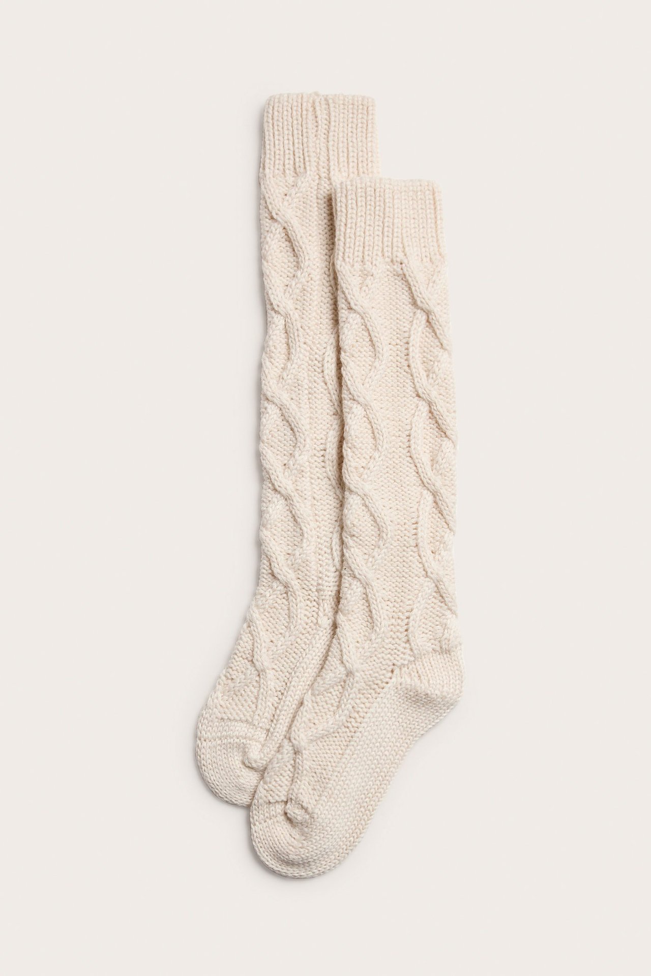 Ovenfra sett par lys beige kabelstrikkede knestrømper i tykt garn.