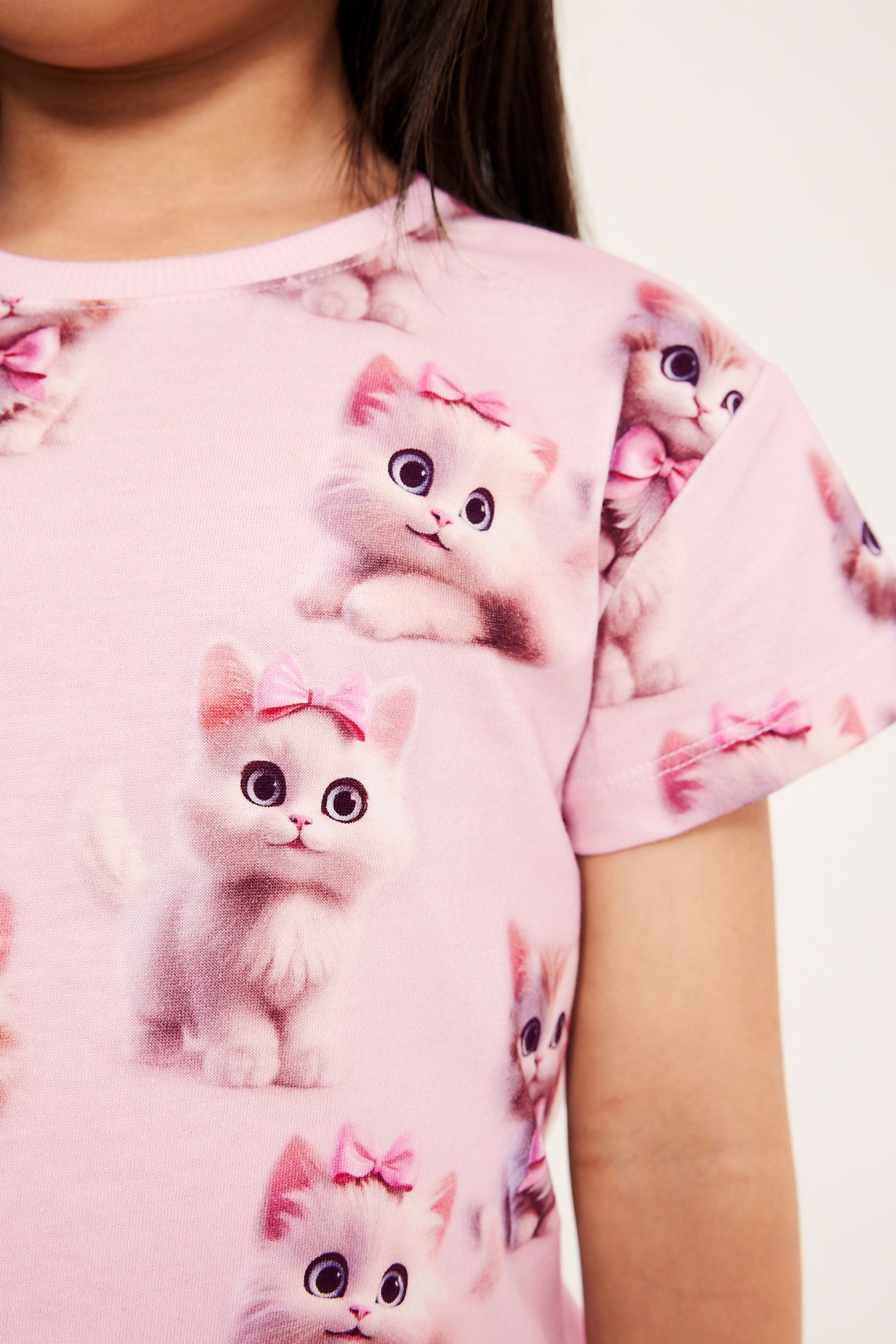 Zbliżenie na dziecko w różowym T-shircie z krótkim rękawem z wzorem białych kotków i różowymi kokardkami.