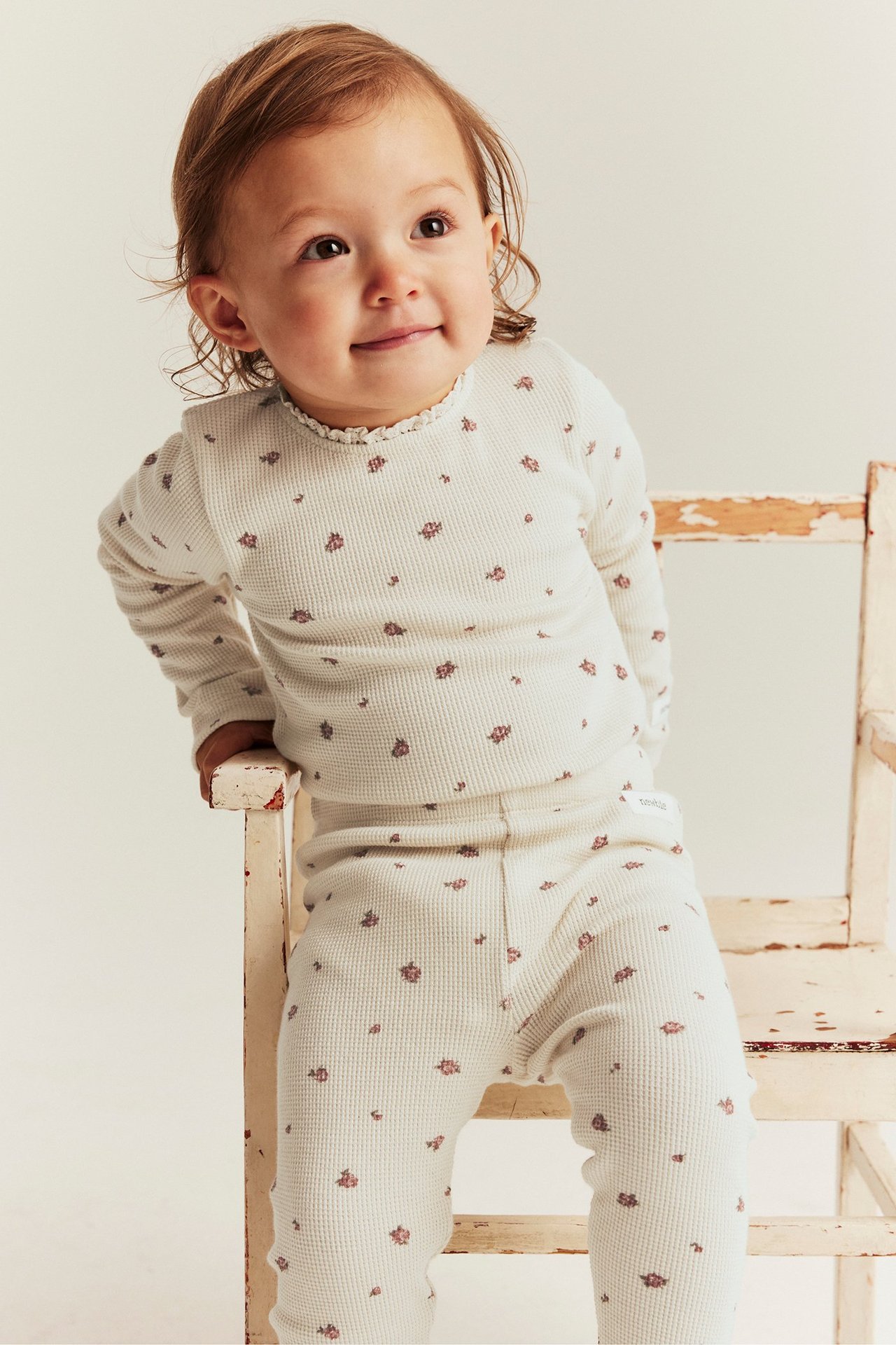 Edestä: vauva yllään vaaleanbeige vohvelineulottu kukkakuvioinen body pitsireunuksella ja yhteensopivat leggingsit.