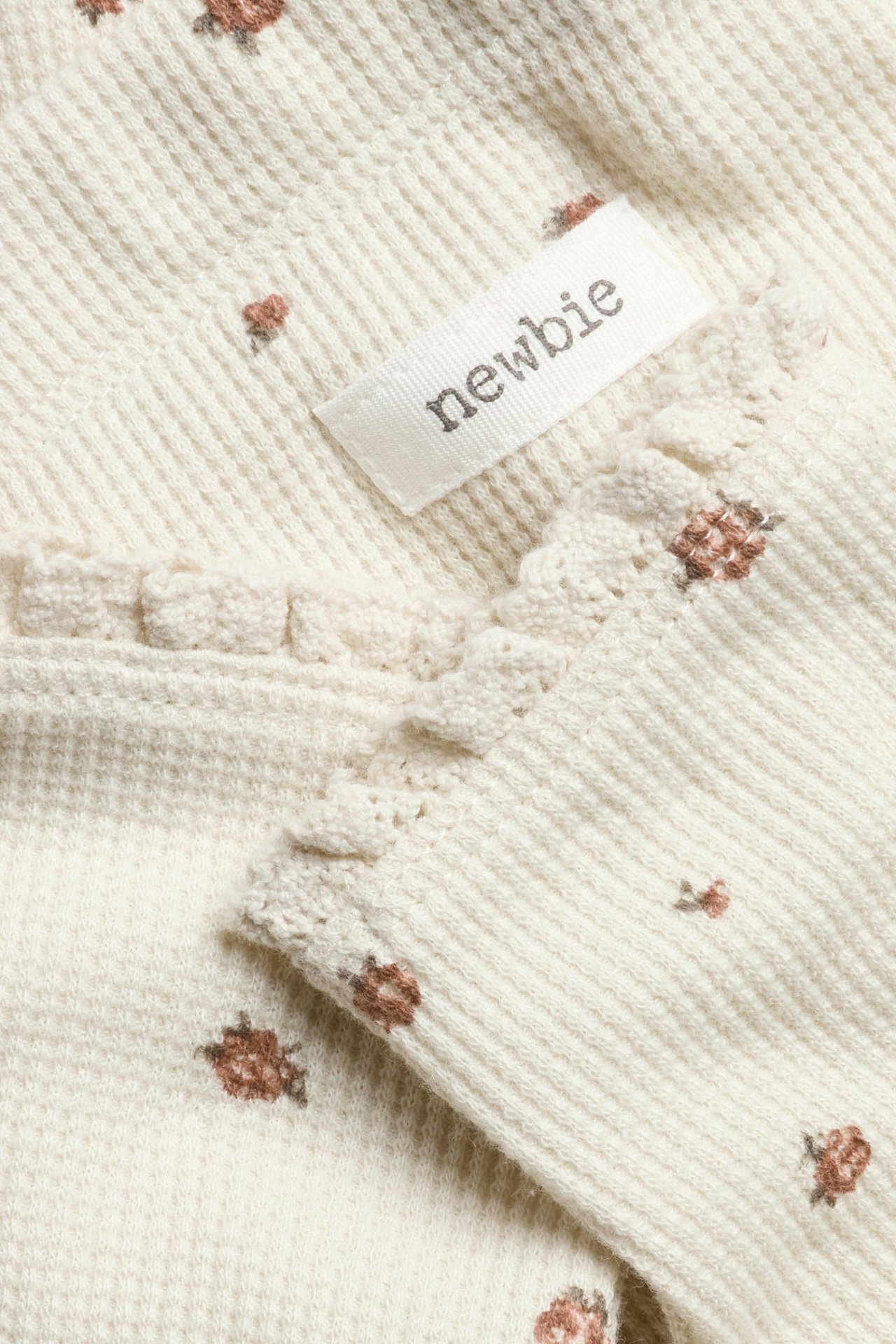 Lähikuva: Vaaleanbeiget vohvelineuleleggingsit pienellä ruskealla kukkakuviolla, pitsireunalla ja Newbie-etiketillä.