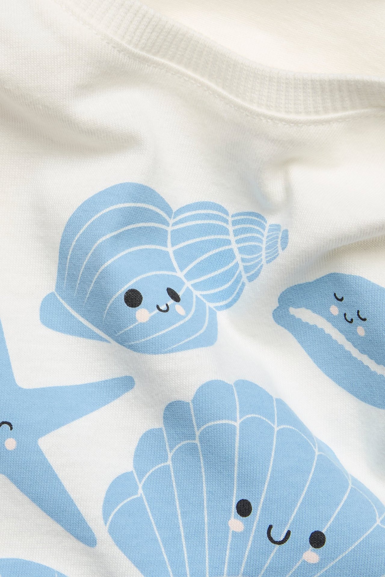 Zbliżenie na białą bawełnianą koszulkę z niebieskim nadrukiem uśmiechniętych stworzeń morskich.