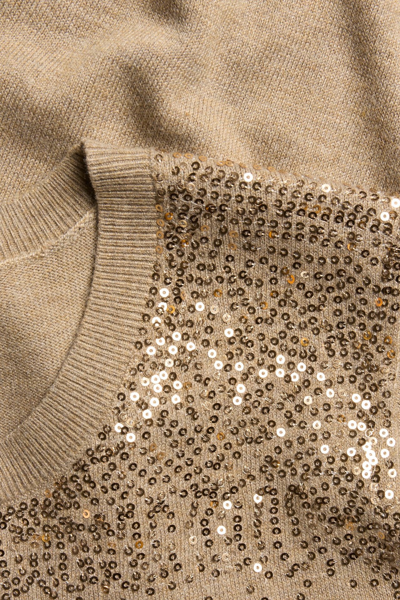Zbliżenie beżowego melanżowego swetra z dzianiny z błyszczącymi złotymi cekinami i prążkowanym dekoltem.