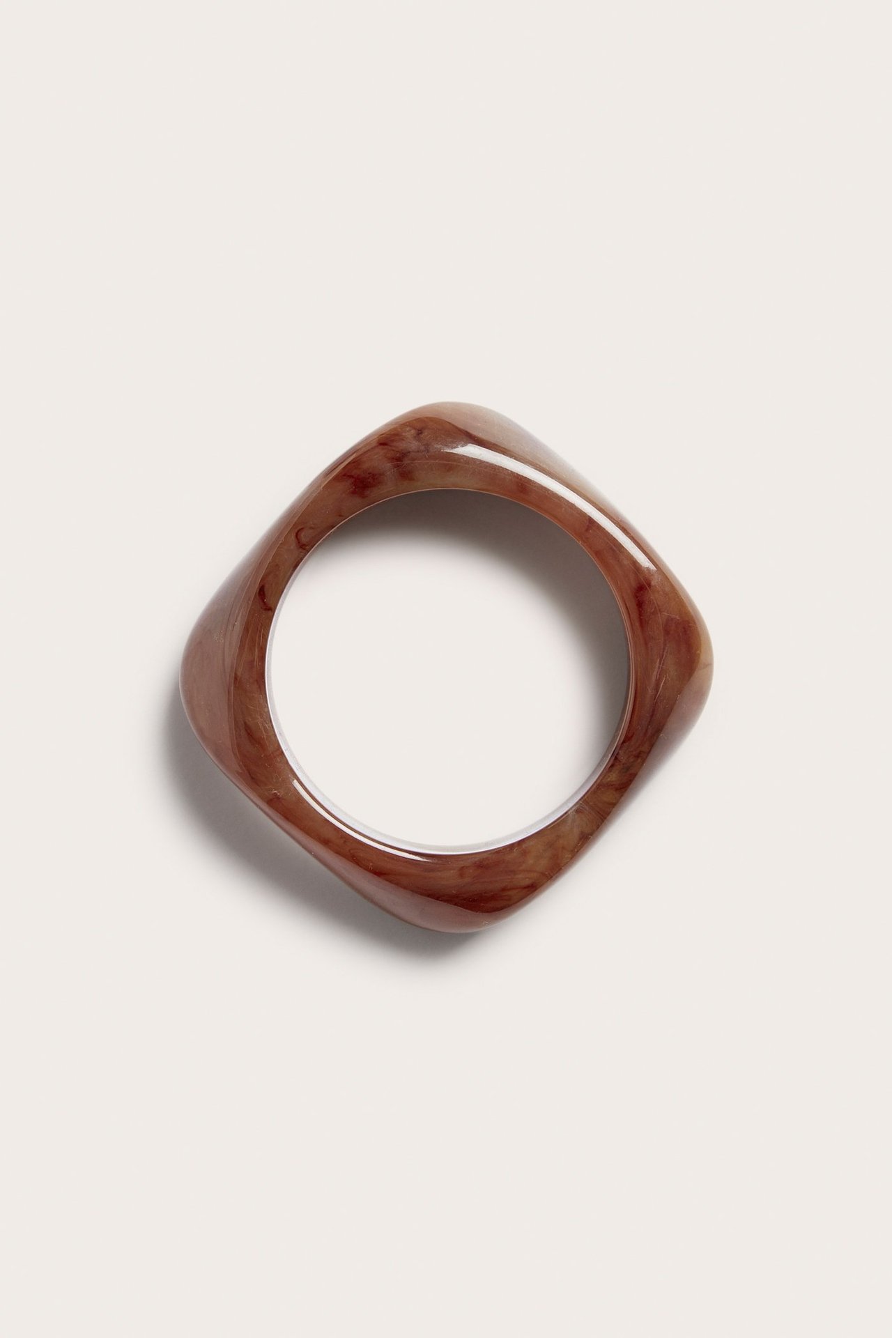 Ovenfra sett brunt marmorert plastarmbånd med avrundet kvadratisk form.