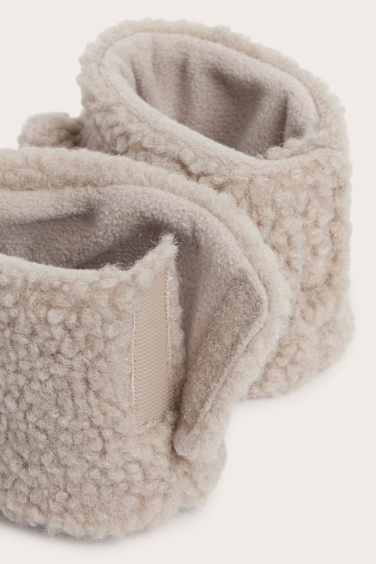 Nærbilde av et par beige babytøfler i mykt pilestoff med borrelåsfeste.