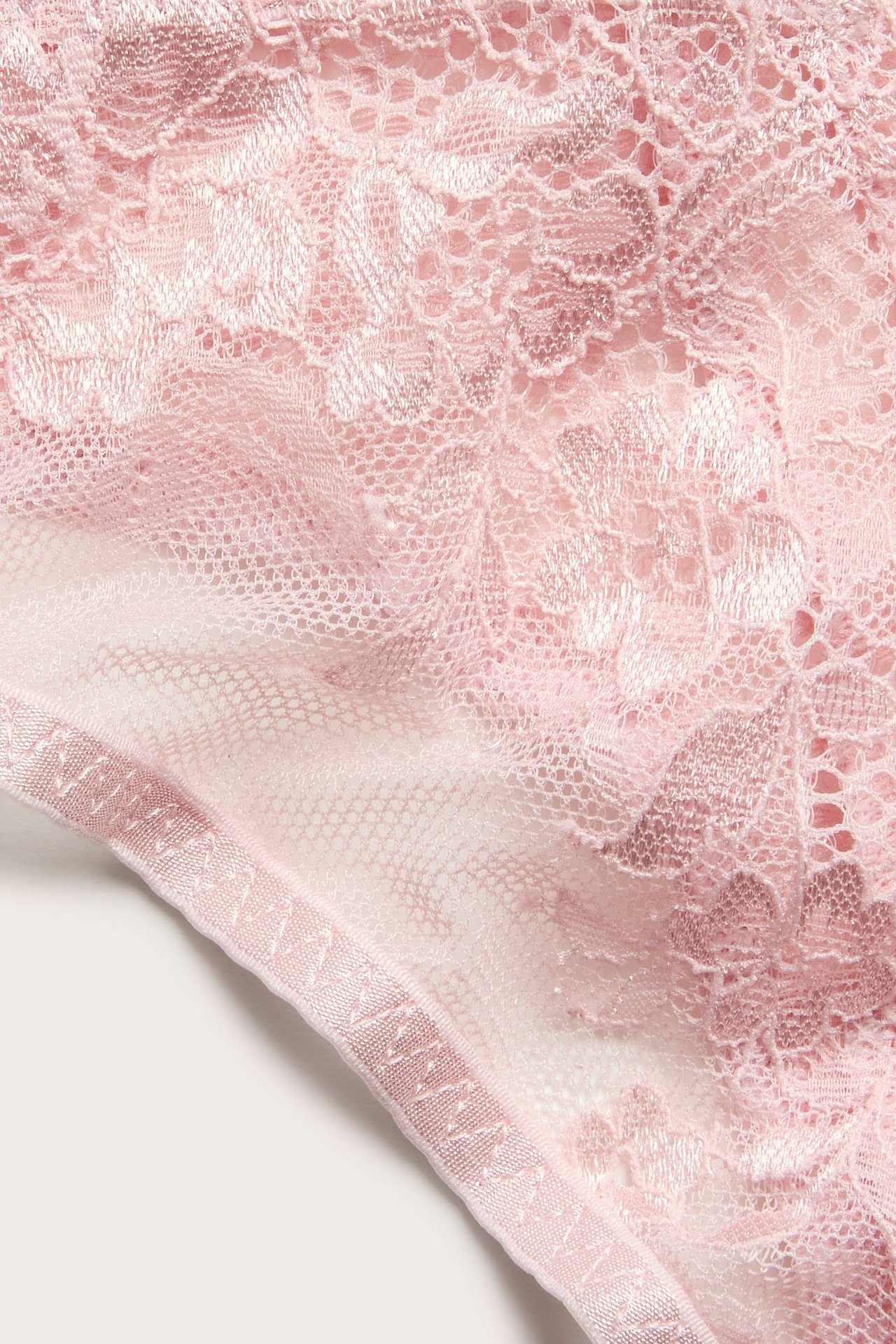 Nærbilde av en lys rosa blondestringtruse med delikat blomstermønster.