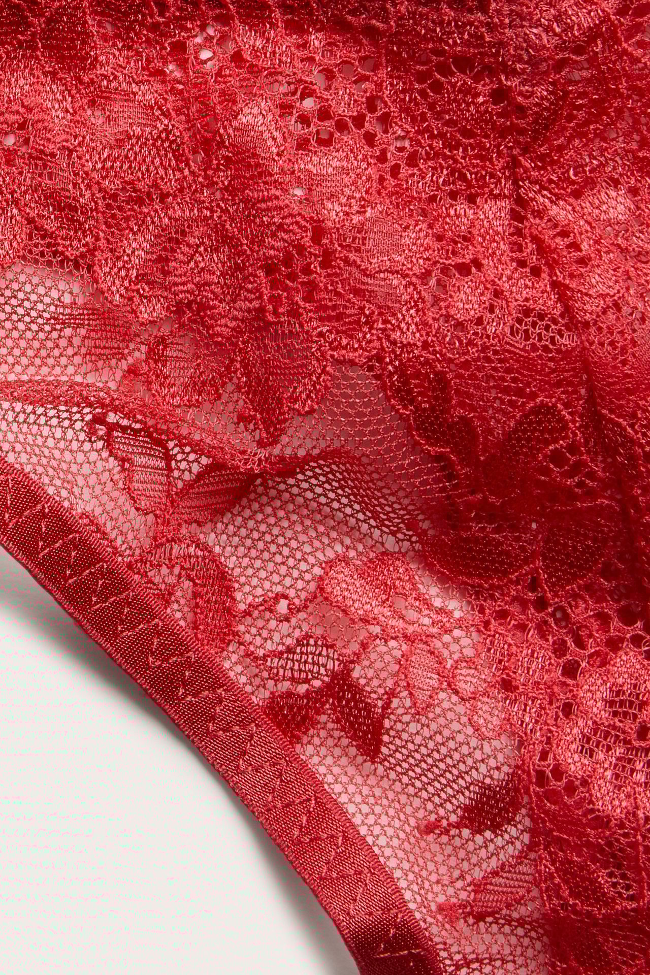 Nærbilde av røde blondestrings med detaljert blomstermønster og delikat elastisk kant.