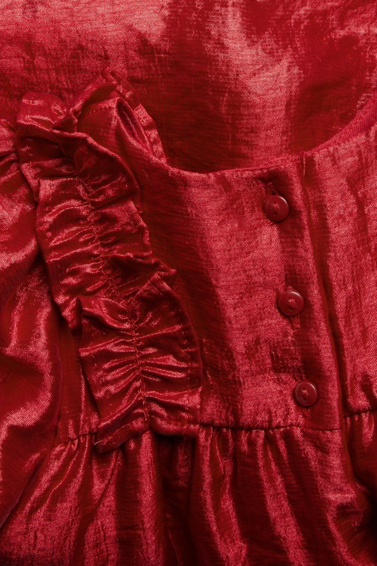 Zbliżenie na czerwoną błyszczącą sukienkę wiskozową z falbankowym rękawem i trzema guzikami.