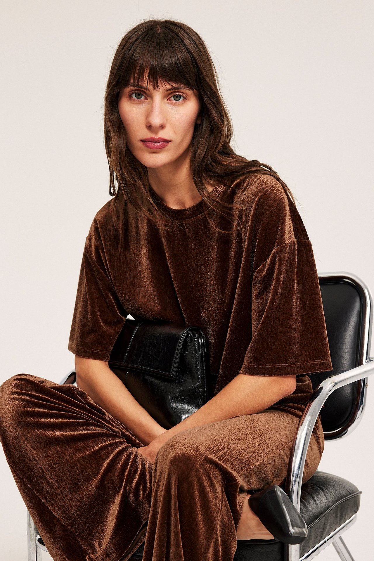 Kvinne i brun velour topp med kortermet, sittende i svart stol.