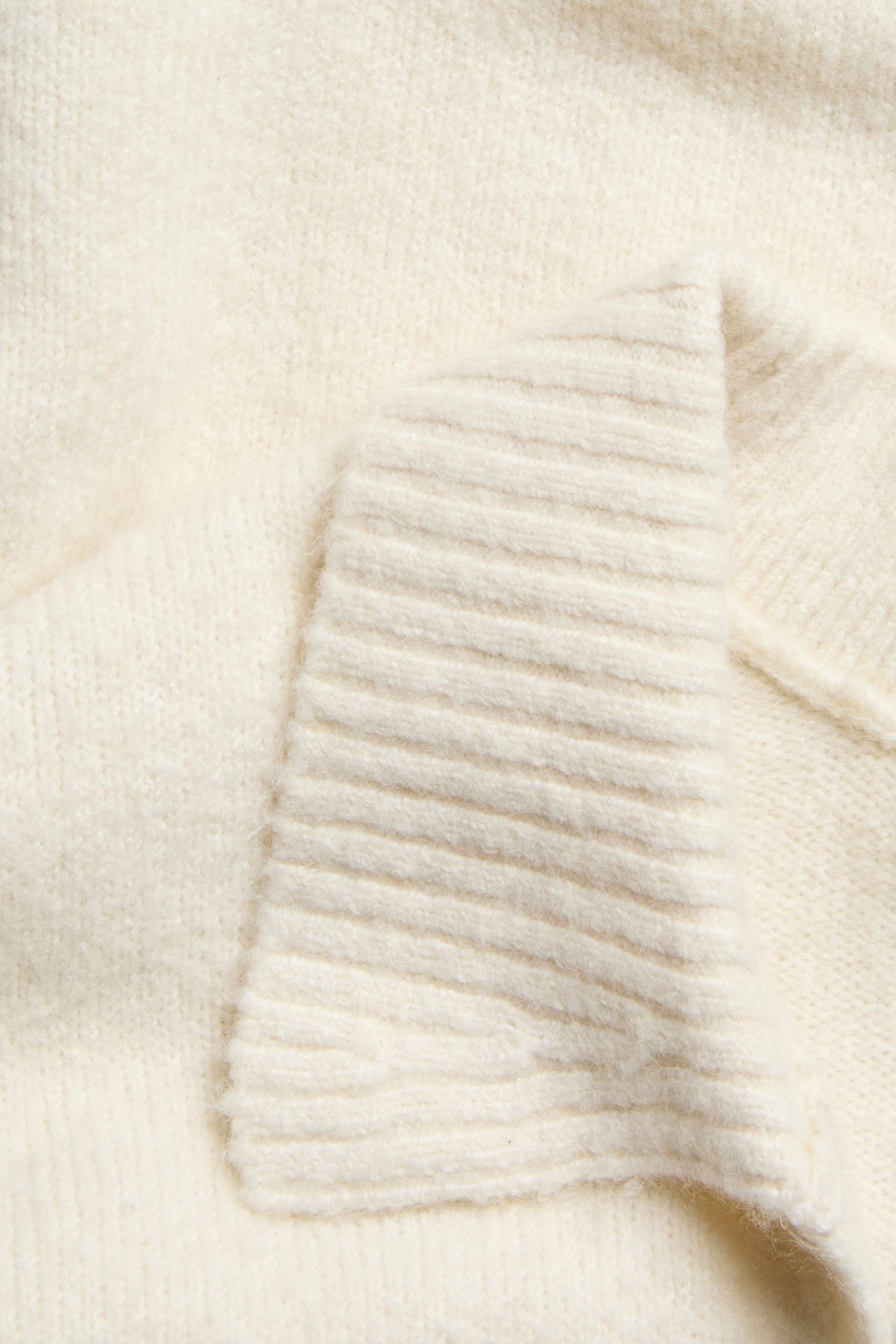 Zbliżenie na miękki, jasnobeżowy melanżowy sweter z dzianiny żeberkowej z kołnierzem.