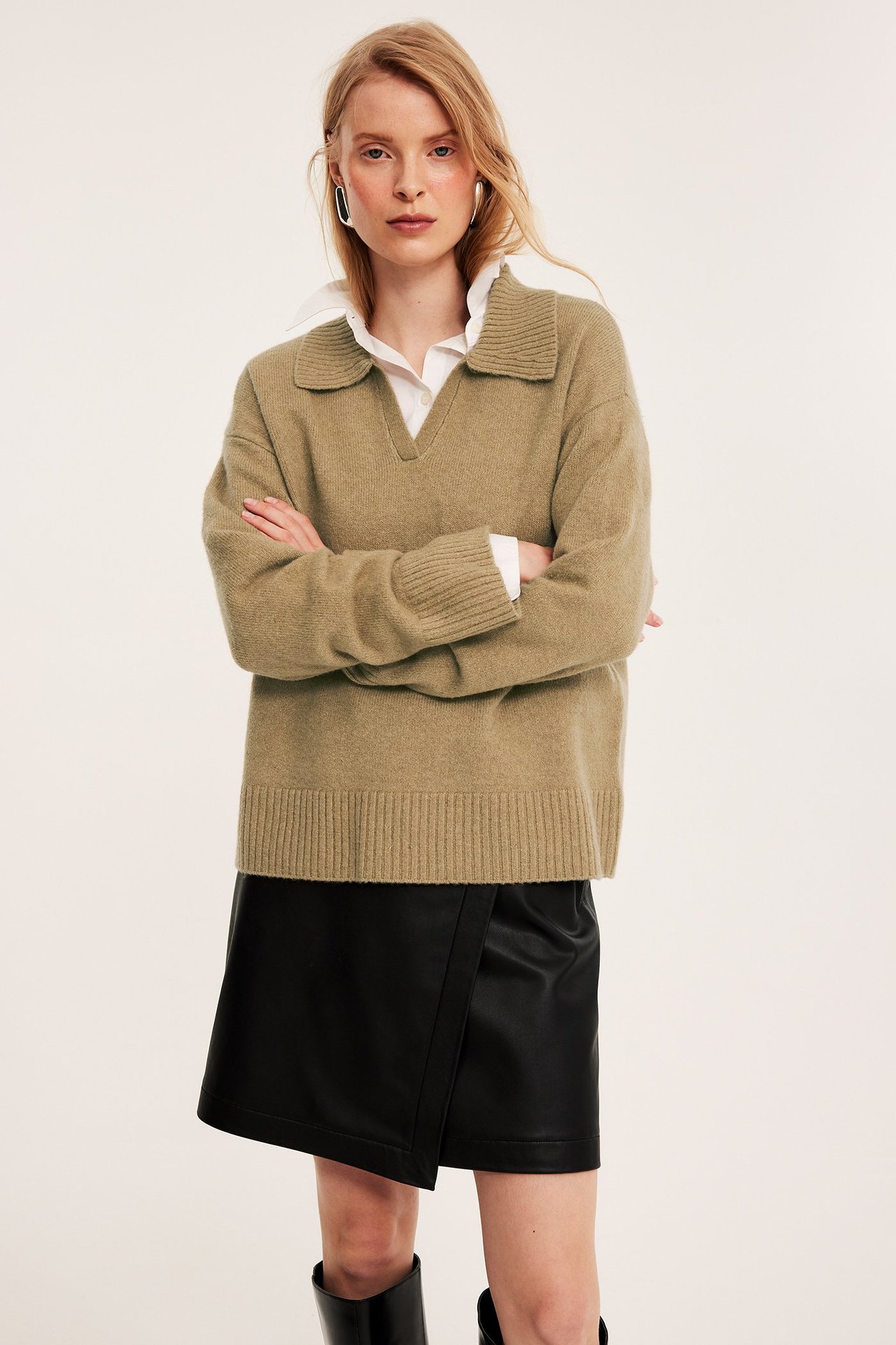 Frontvy, kvinna i beige melerad stickad pullover, vit skjorta och svart fuskläder minikjol.