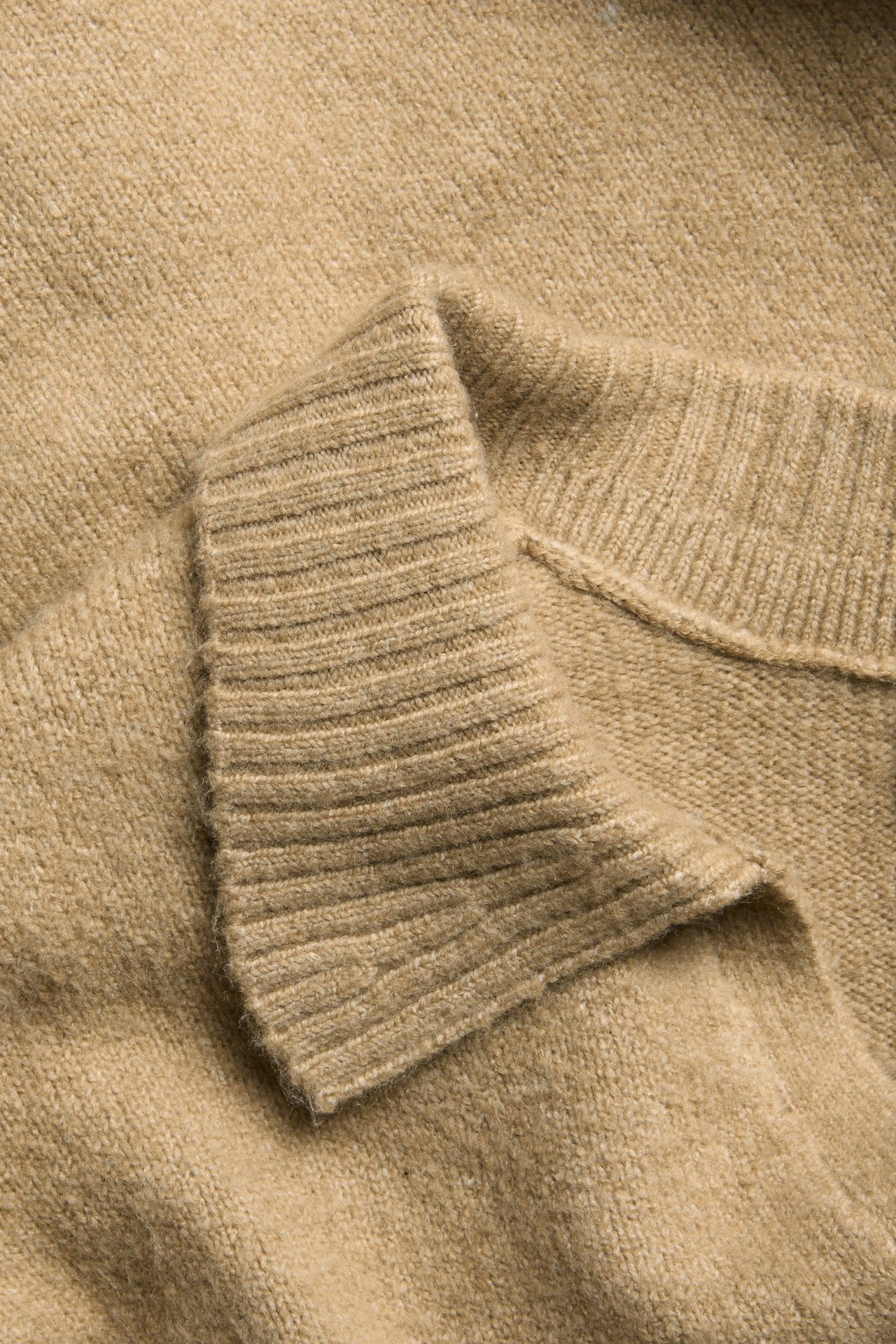 Zbliżenie beżowego, melanżowego swetra z dzianiny z prążkowanym kołnierzem.