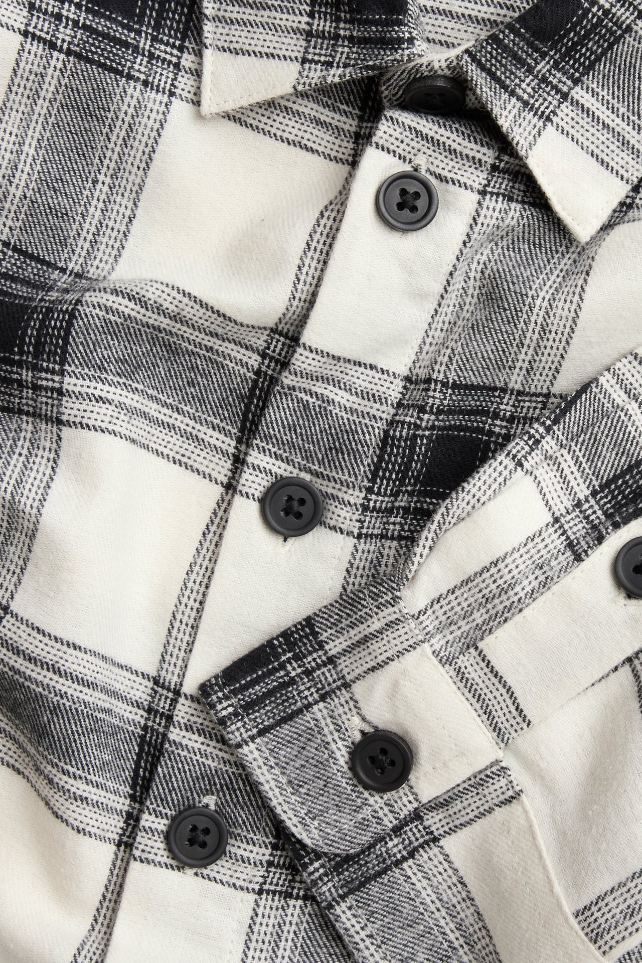 Zbliżenie na dziecięcą koszulę z flaneli bawełnianej w biało-czarną kratę z czarnymi guzikami.