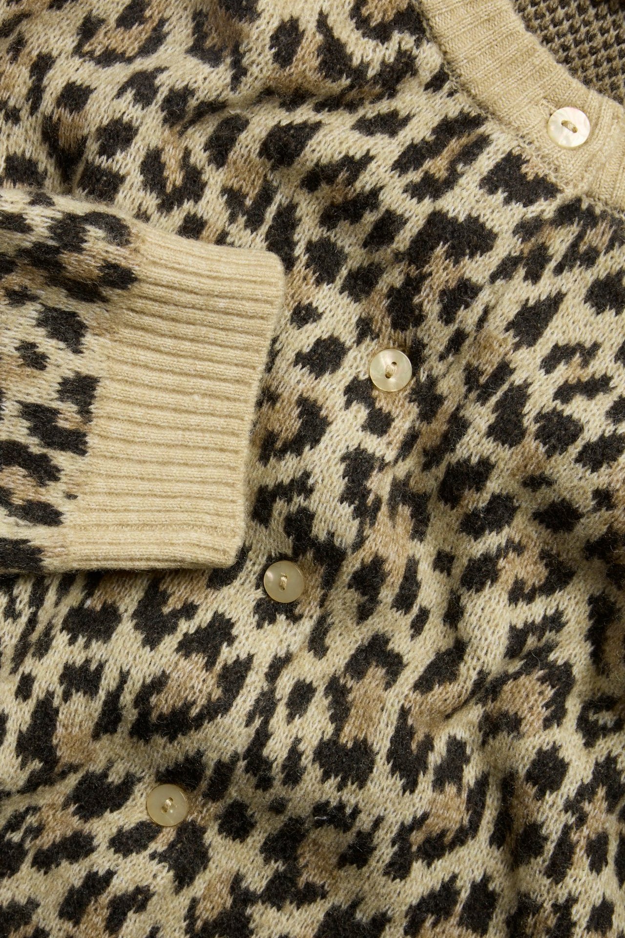 Zbliżenie beżowego kardiganu w żakardowy wzór lamparta z prążkowanymi mankietami i jasnymi guzikami.