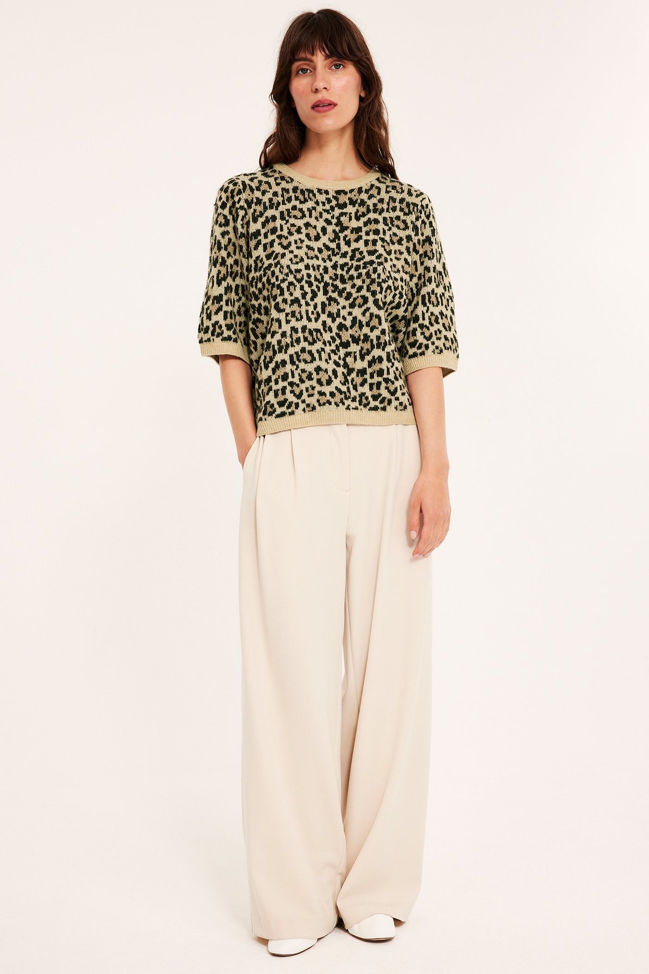 Edestä kuvattu nainen beigessä leopardikuvioisessa neulotussa t-paidassa ja vaaleanbeigessä leveälahkeisissa housuissa.