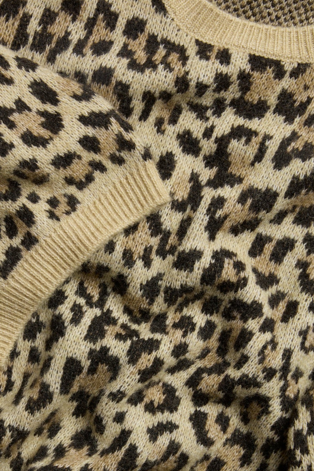 Zbliżenie beżowego dzianinowego T-shirtu z brązowo-czarnym wzorem w panterkę.