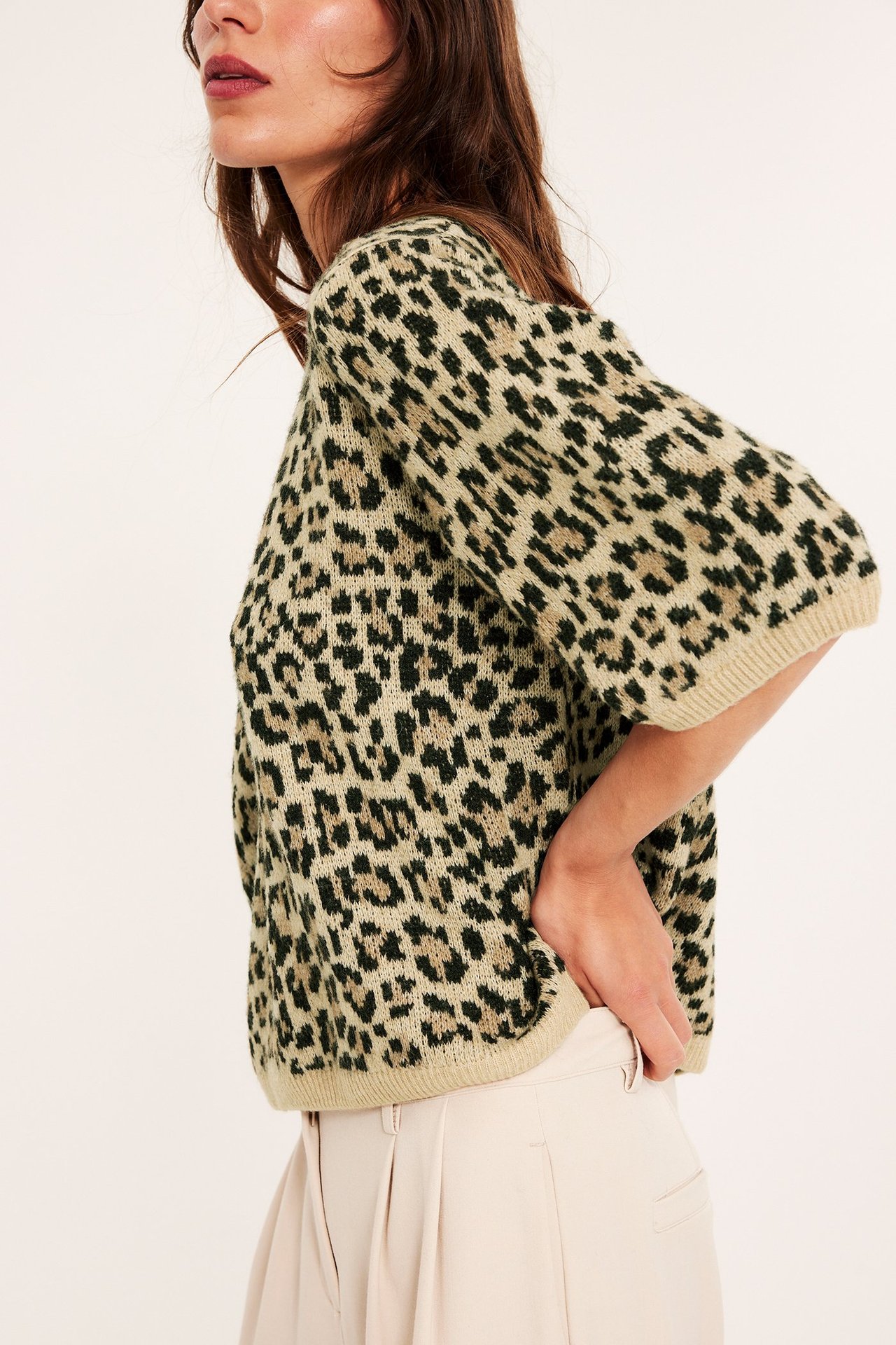 Sivukuva naisesta yllään beige neulottu leopardikuvioinen t-paita ja vaaleanbeiget laskostetut housut.