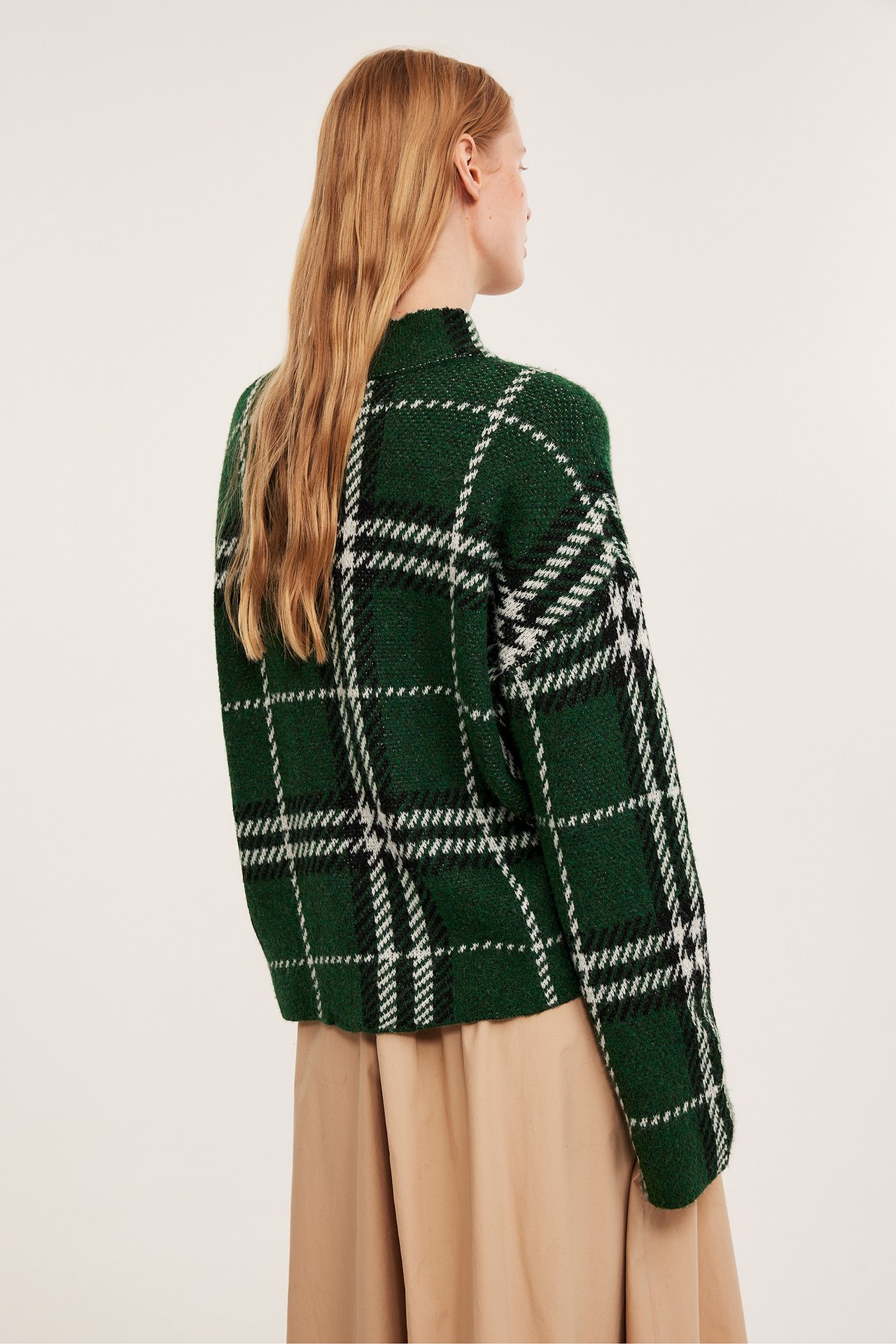 Bakifrån, kvinna i mörkgrön rutig stickad pullover med svarta och vita rutor över en beige kjol.