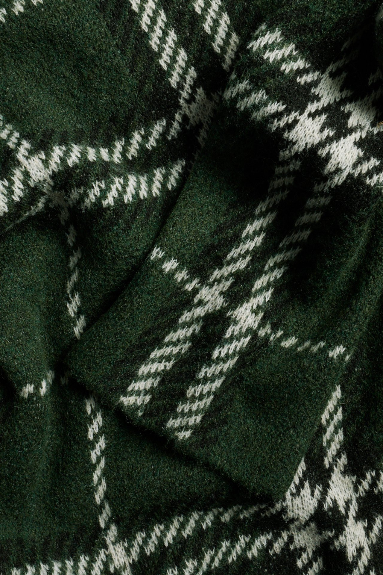Närbild av en mörkgrön stickad pullover med vitt rutigt mönster.