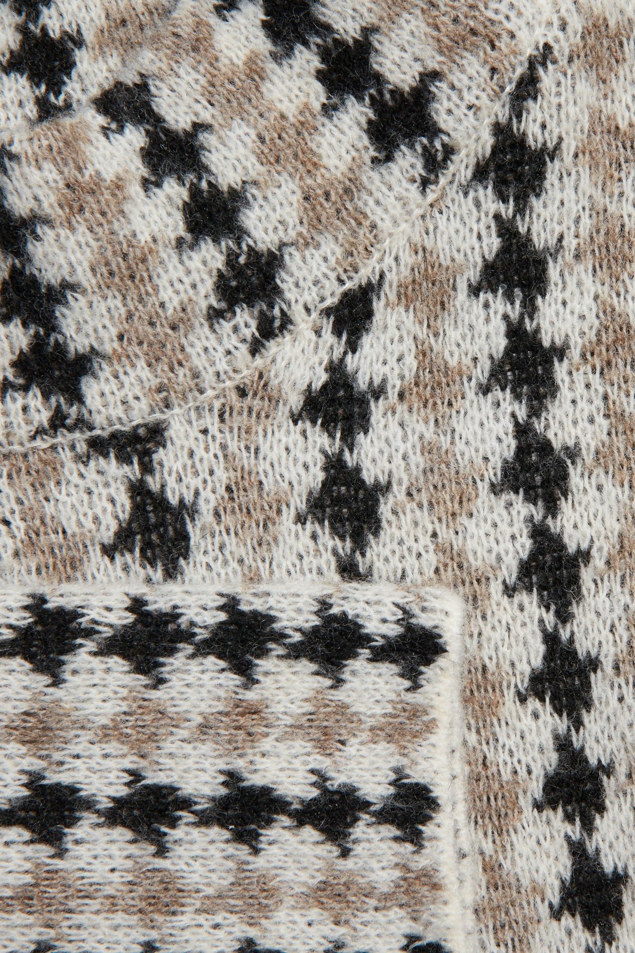 Zbliżenie na jasnobeżowy, czarno-biały wzorzysty sweter dzianinowy w pepitkę.