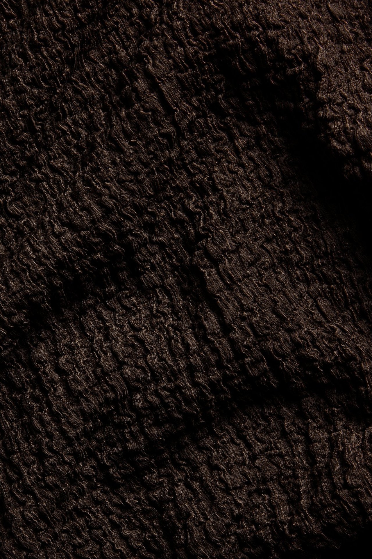 Zbliżenie na ciemnobrązowy, teksturowany materiał obszernego t-shirtu.