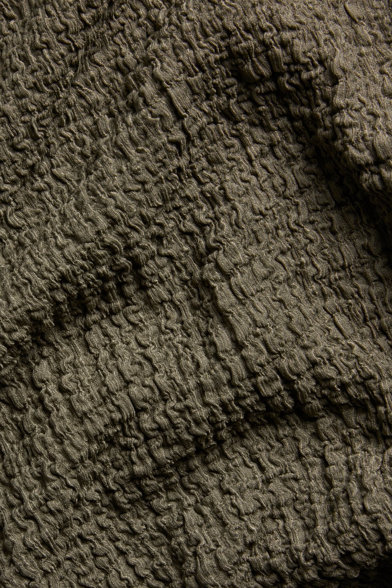 Zbliżenie na ciemnobrązowy, teksturowany materiał na koszulkę oversize.