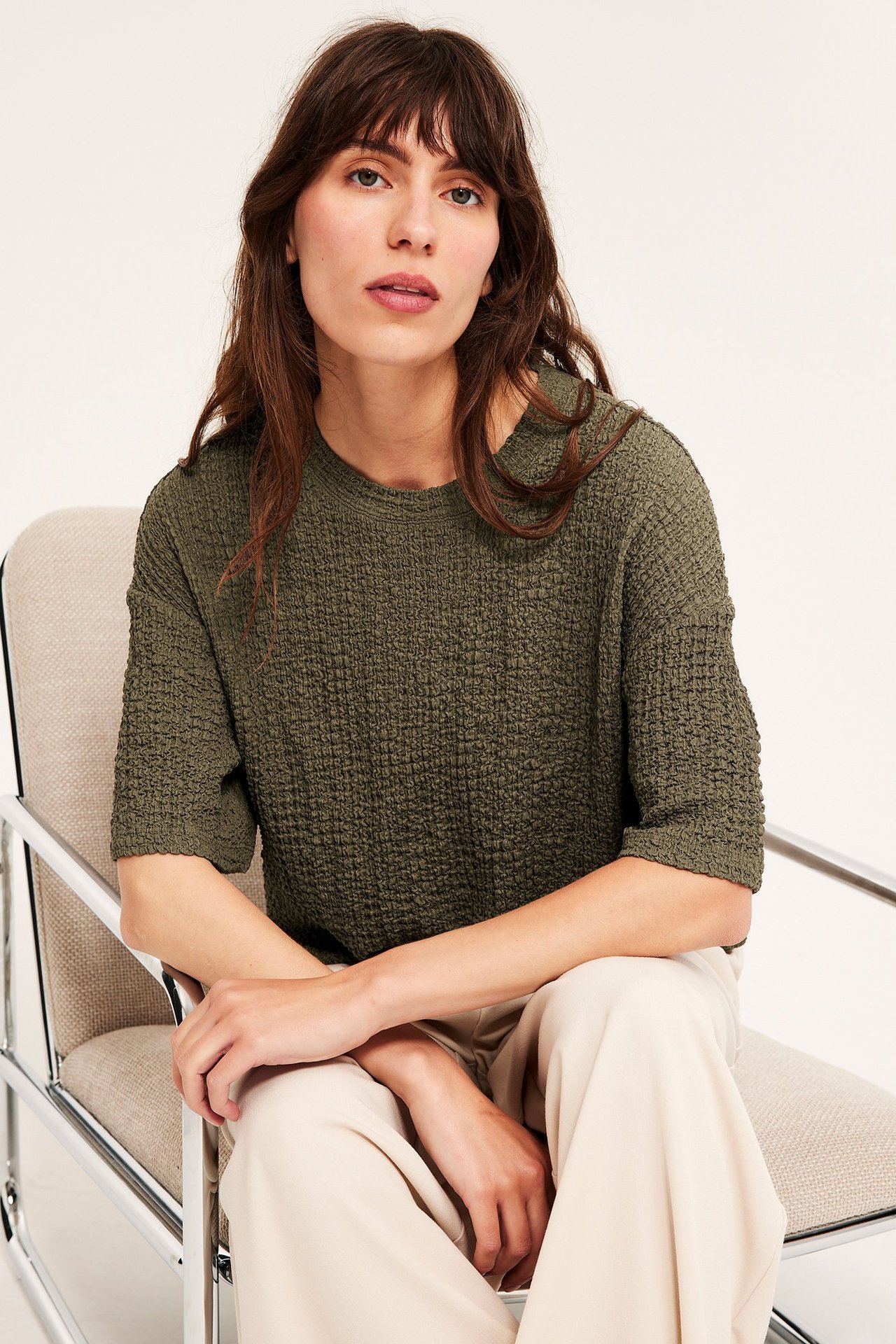 Widok z przodu: kobieta w ciemnozielonym, oversize'owym, teksturowanym T-shircie i jasnobeżowych szerokich spodniach.