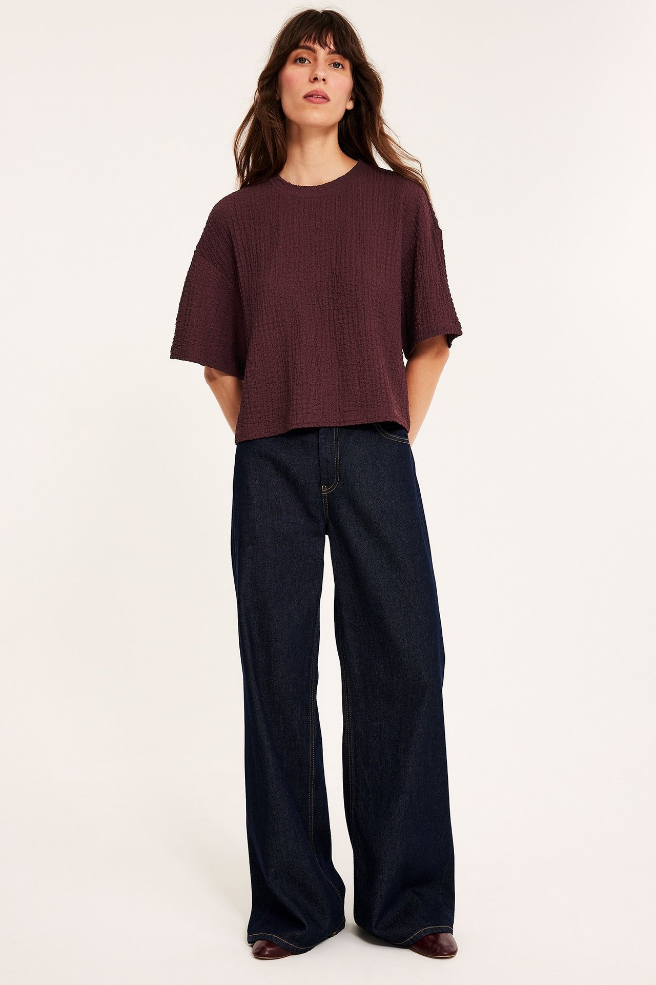 Kvinne har på seg en forfra mørkerød strukturert oversized t-skjorte, mørkeblå vide jeans og mørkerøde sko.