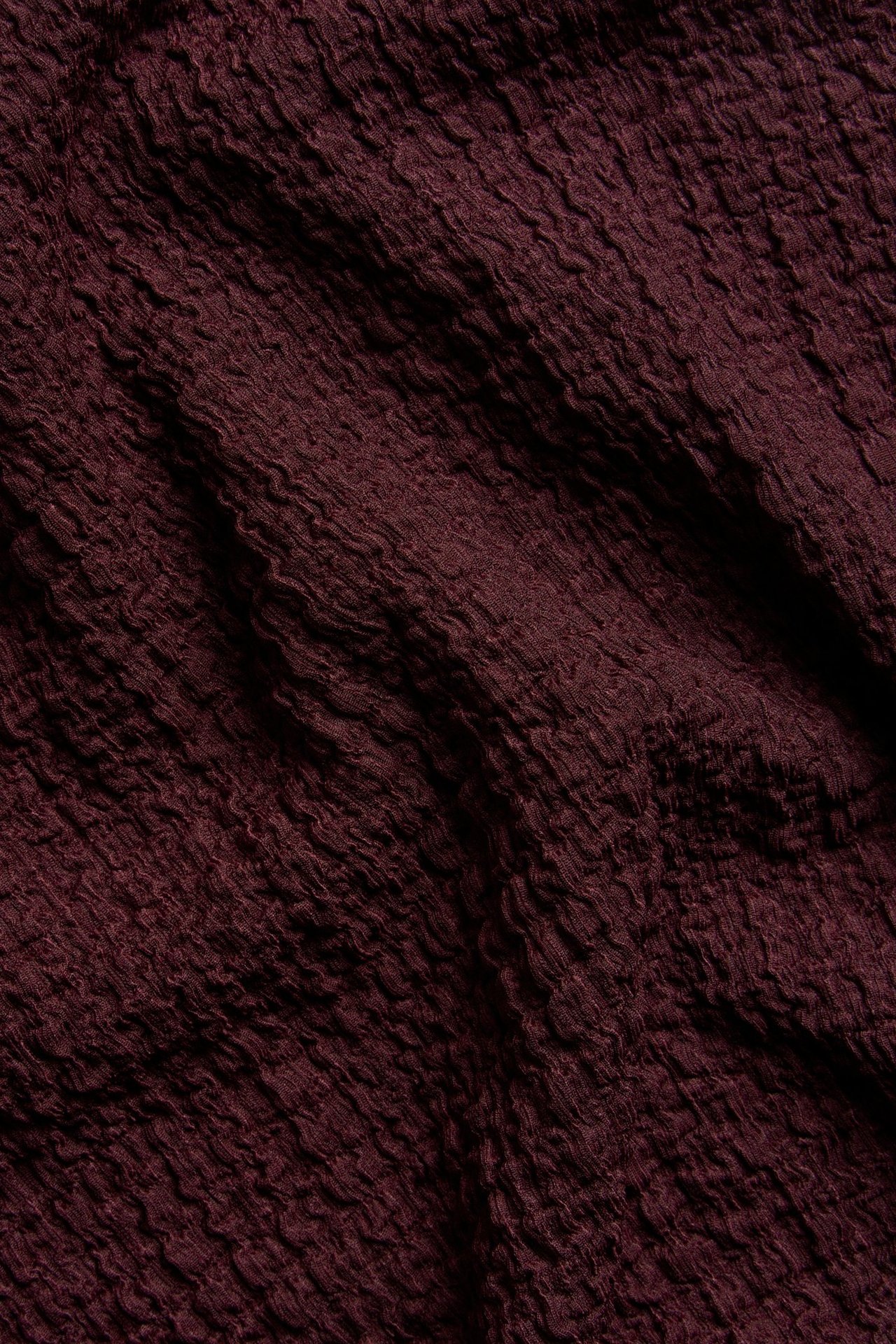 Zbliżenie na ciemnoczerwony, teksturowany materiał na koszulkę oversize, ukazujące jego strukturę.