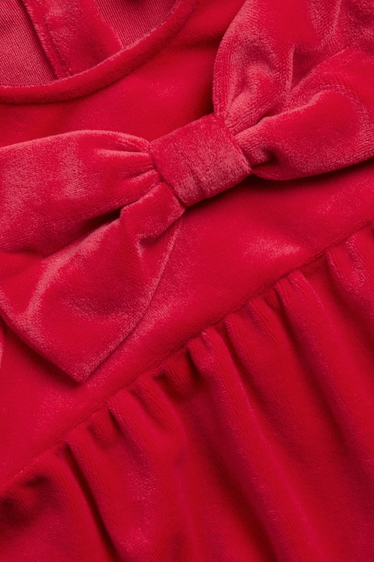 Zbliżenie na czerwoną welurową sukienkę niemowlęcą z dużą kokardą z przodu.