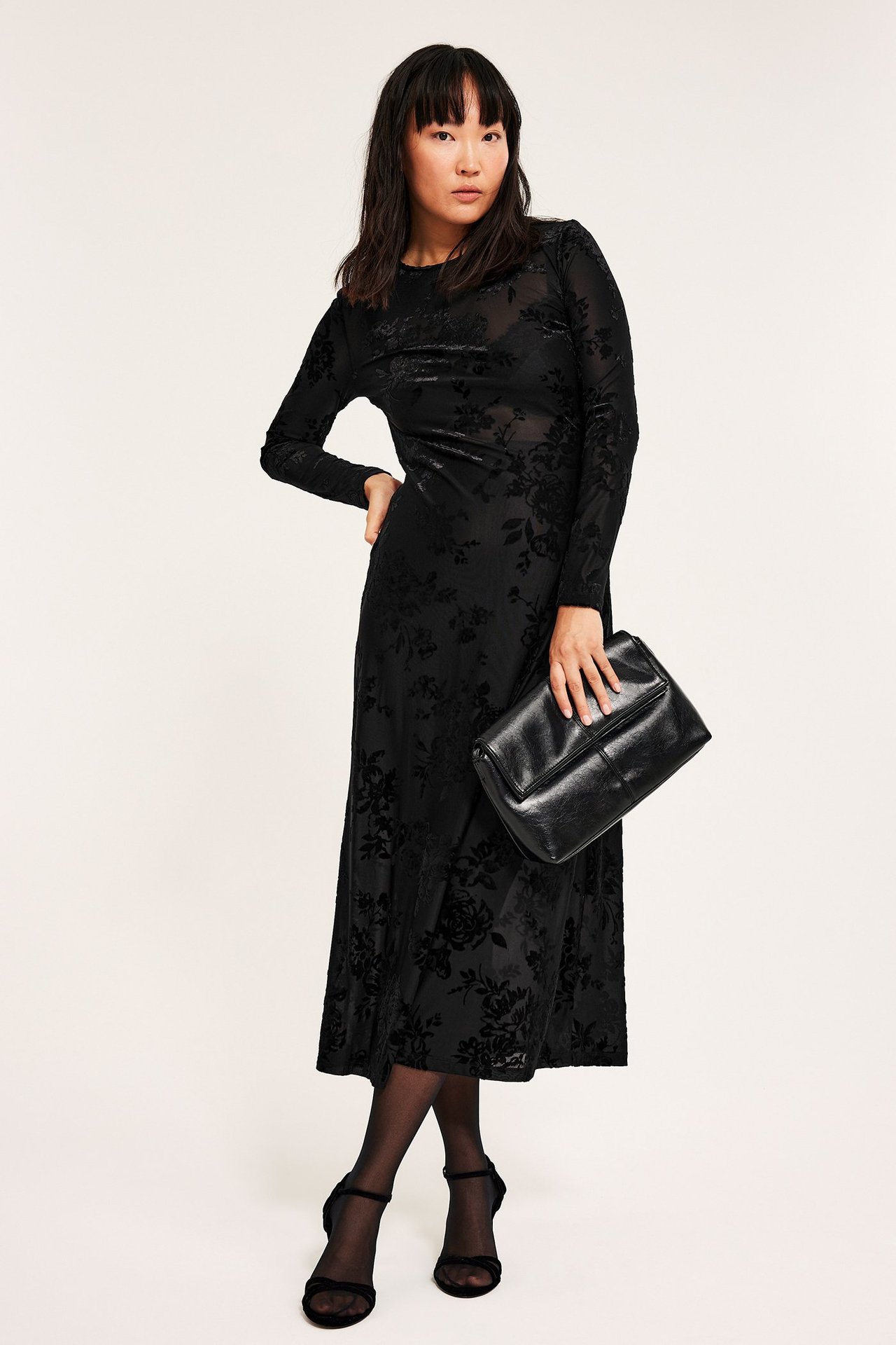 Kvinne i svart blomster flockprint maxiklänning, uten slip, tettsittende, holder svart veske.