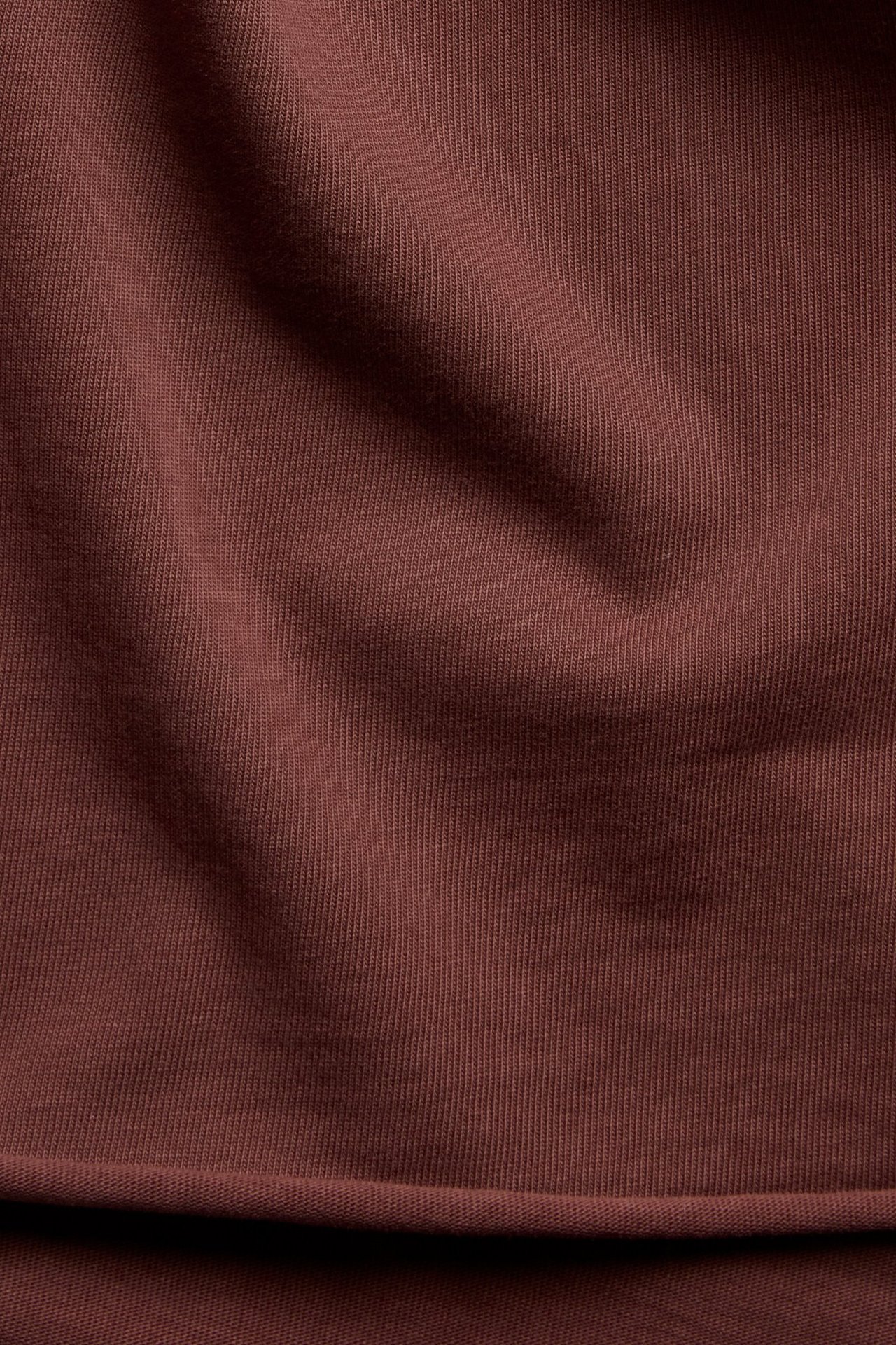 Zbliżenie na bordowy, jednolity materiał z bawełnianej dzianiny, prawdopodobnie na top z dekoltem w serek.