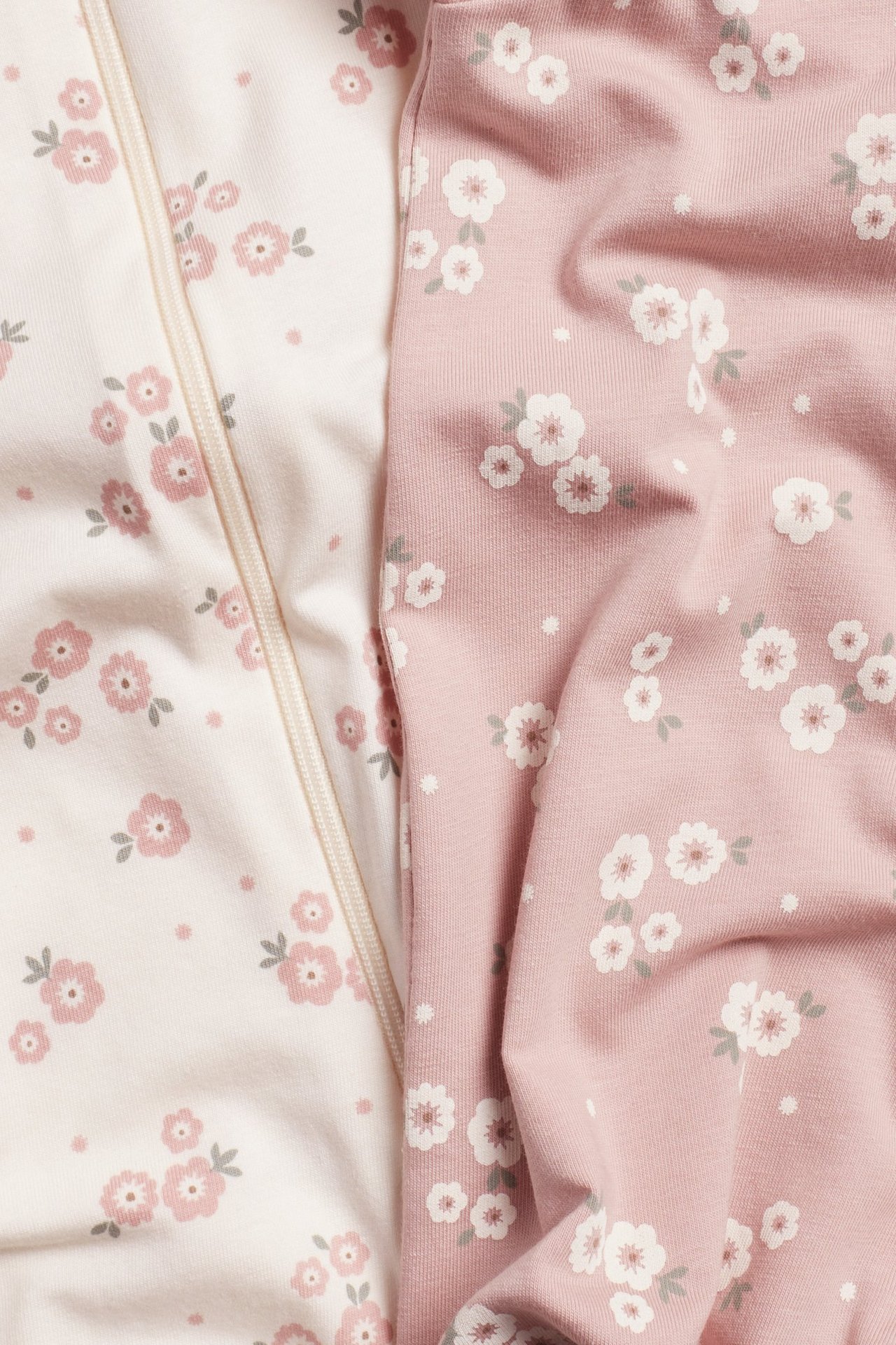 Zbliżenie: dwa pajacyki niemowlęce, jasnoróżowy i różowy, oba w kwiaty, z zamkiem błyskawicznym.