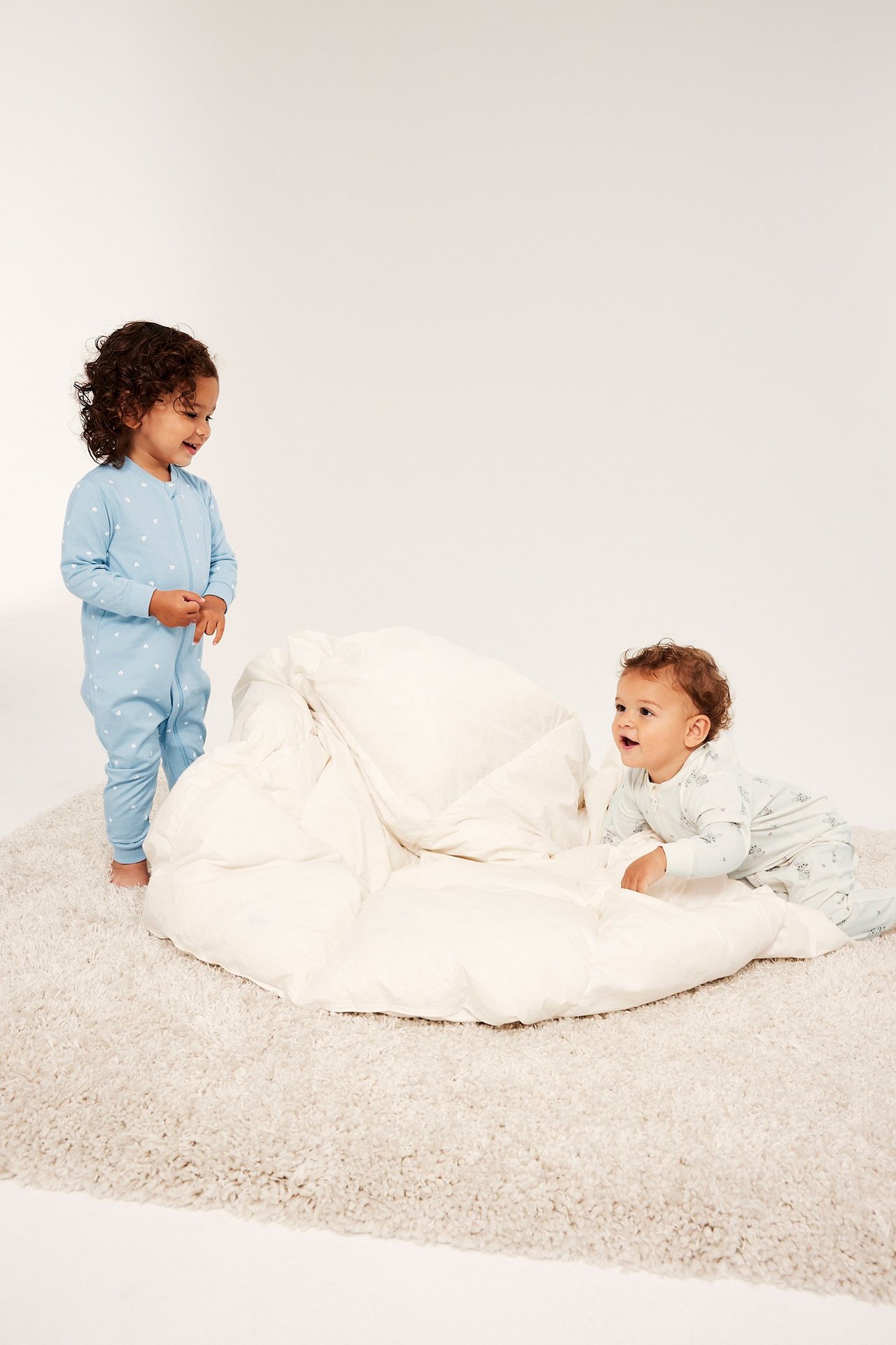 Forfra, to babyer i mønstrete pyjamaser: én lyseblå med hjerter, én off-white med kaniner.
