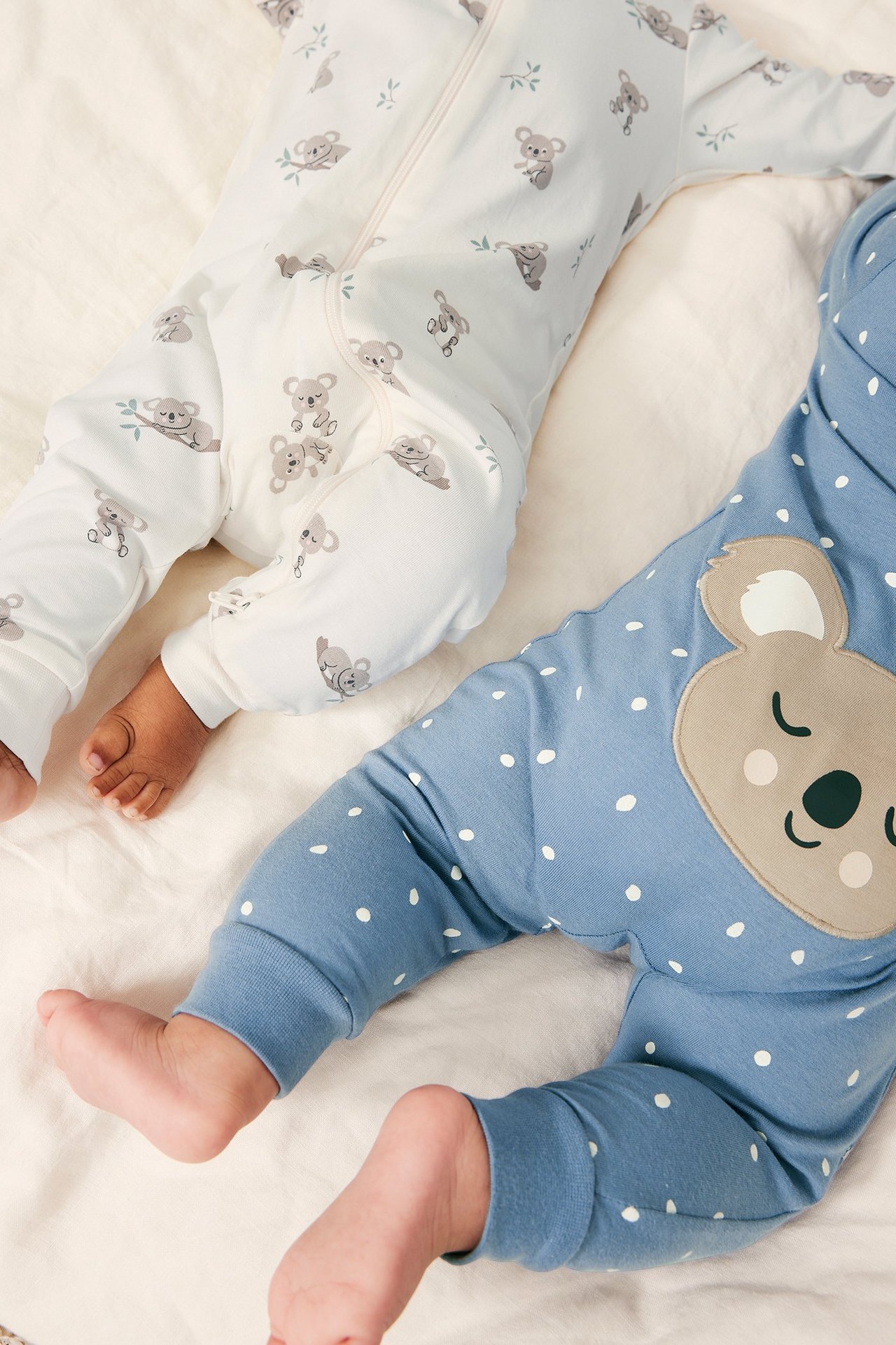 Nærbilde av to babyer: off-white koala-heldress og blå prikkete heldress med koala-applikasjon.