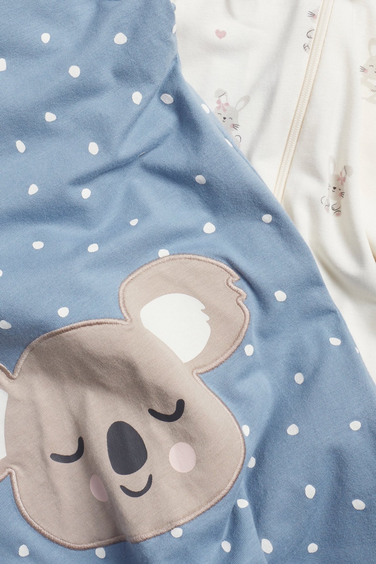 To babypyjamaser: en blå med koala-applikasjon, og en off-white med kanintrykk og toveis glidelås.
