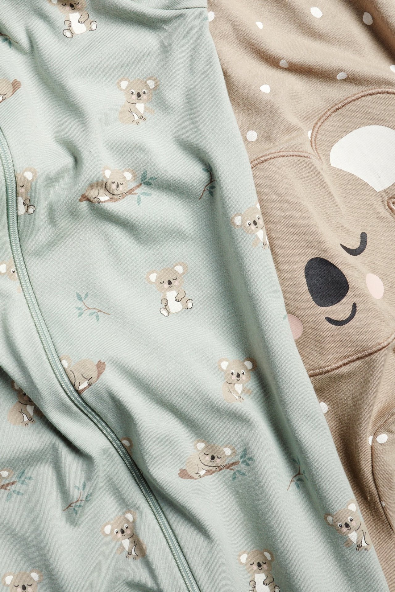 Zbliżenie na jasnozielony pajac niemowlęcy w misie koala z zamkiem, obok beżowego pajaca z misiem.