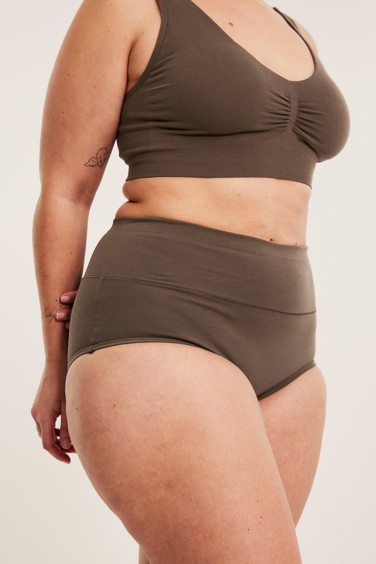 Widok z boku kobiety w ciemnobrązowych hipsterach z szerokim pasem i pasującym biustonoszem.