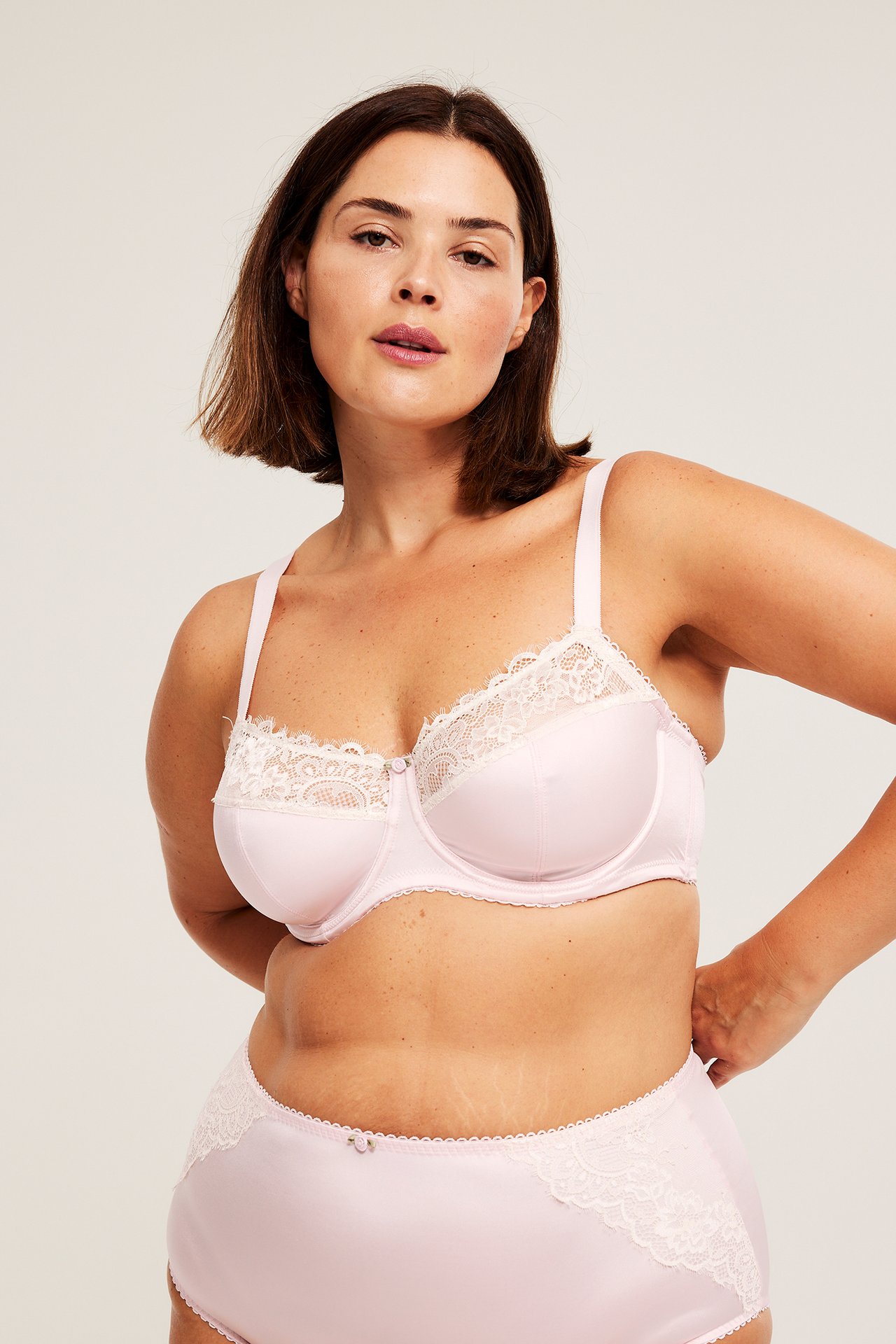Frontbilde av kvinne i lyserosa sateng-BH med spiler, med hvit blonde og matchende truse.